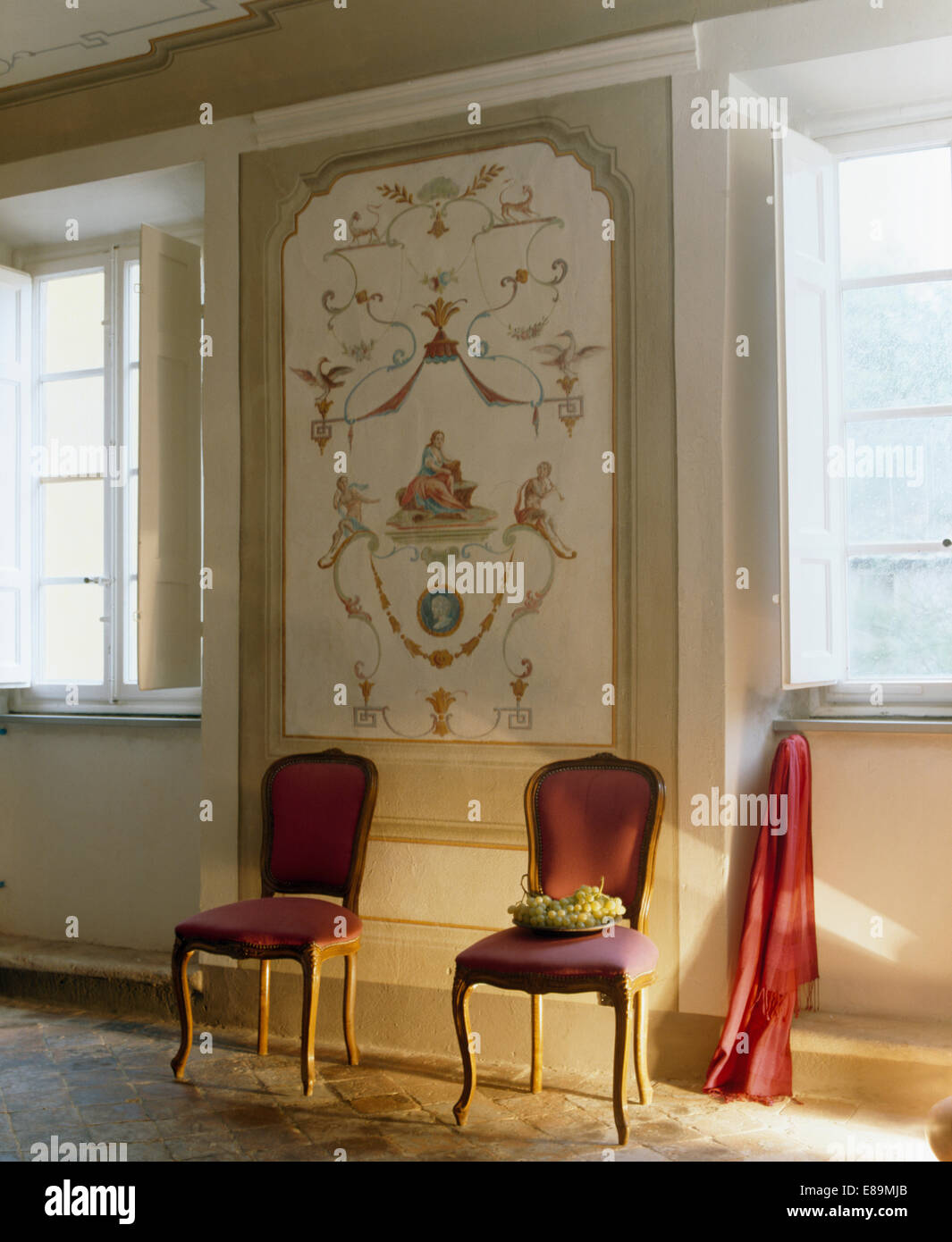 Zwei rote Stühle gegen Wand mit dekorativ Panel im toskanischen Salon mit weißen Fensterläden gemalt. Stockfoto