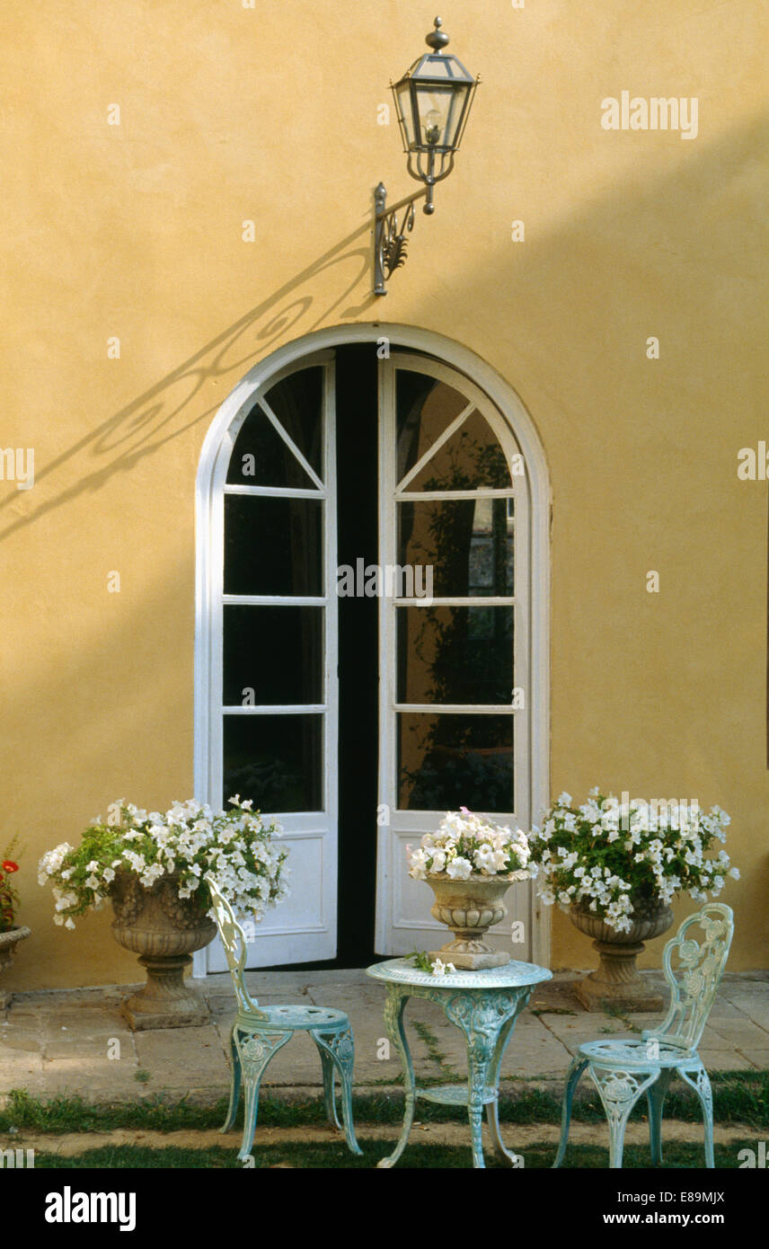 Schmiedeeisen Tisch mit passenden Stühlen vor italienische Villa mit weißen Petunien in Steinurnen auf beiden Seiten der Glastür Stockfoto