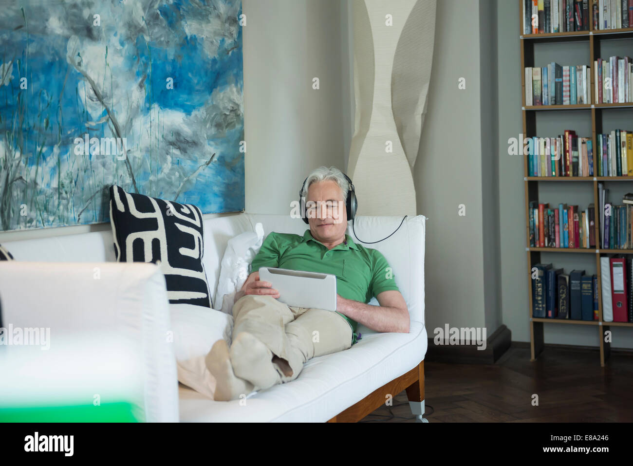 Reifer Mann mit Kopfhörer und digital-Tablette auf Couch sitzen, Lächeln Stockfoto