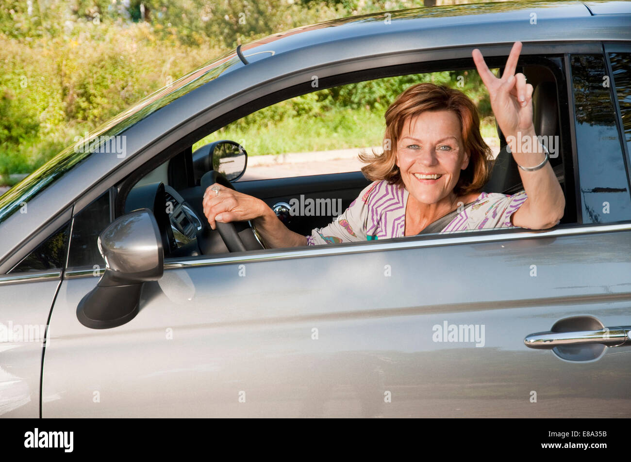 Ältere Frau sitzt im Auto und zeigt Victory-Zeichen Stockfoto