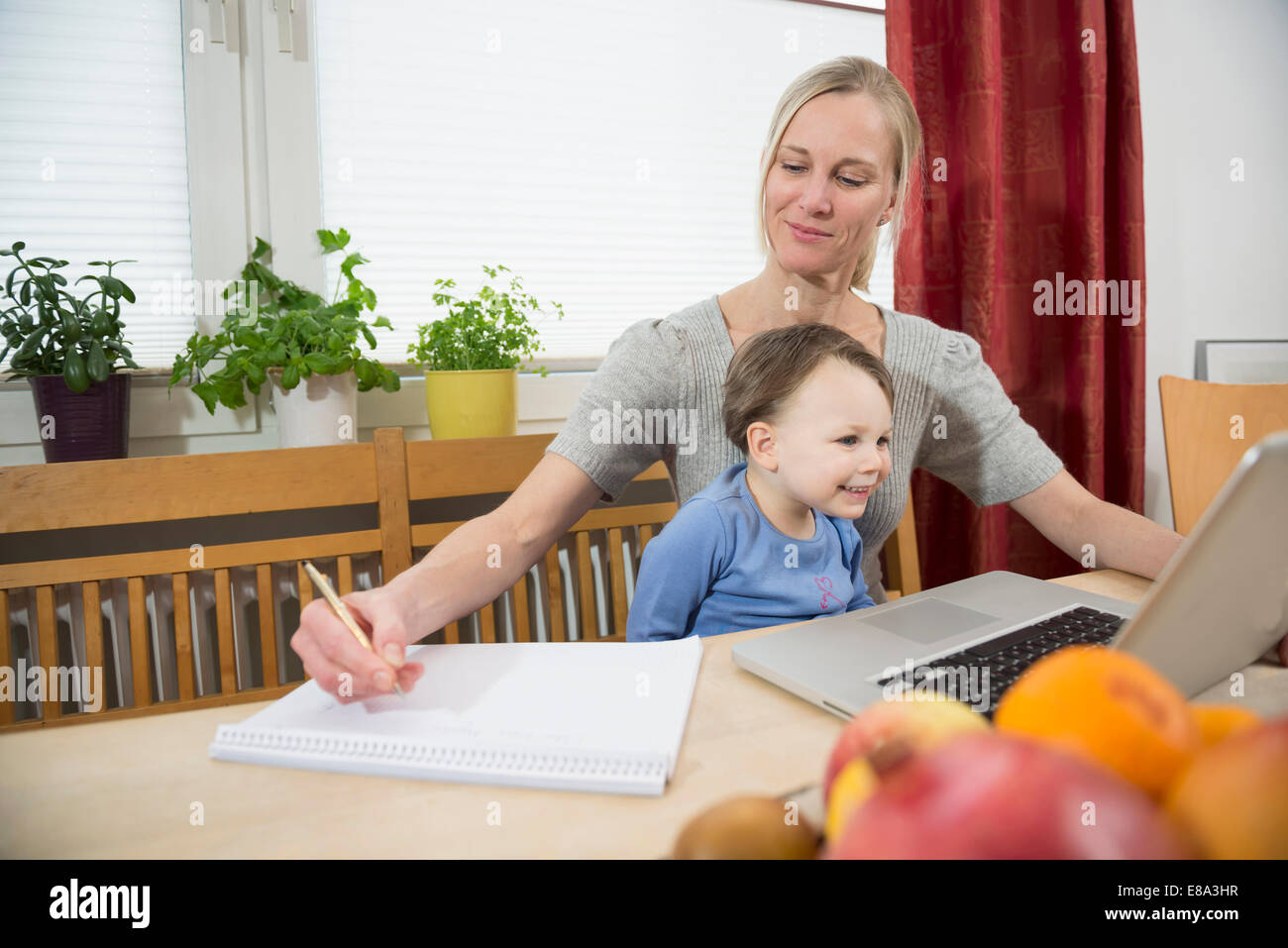 Mutter und Sohn mit Laptop während der Notizen, Lächeln Stockfoto