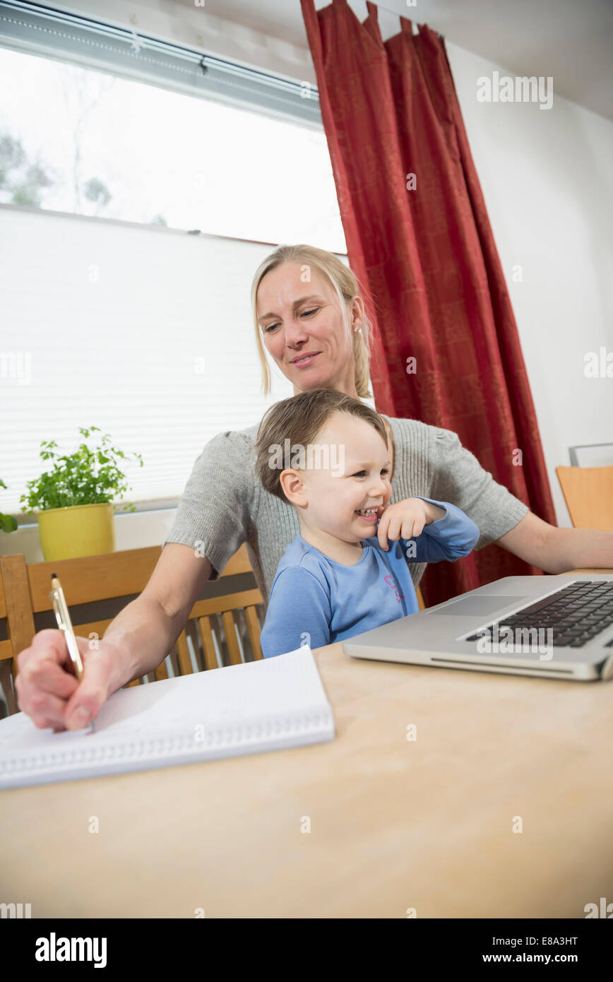 Mutter und Sohn mit Laptop während der Notizen, Lächeln Stockfoto