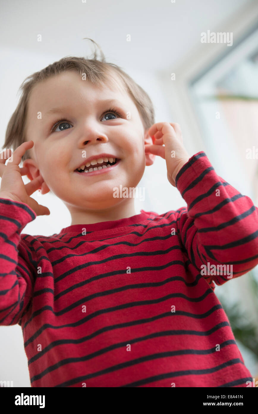Junge mit den Fingern in den Ohren, Lächeln Stockfoto