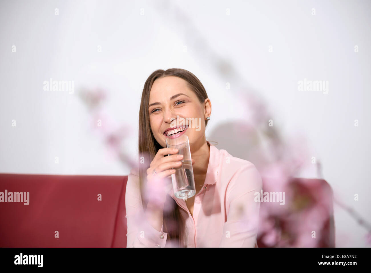 Junge Frau Sofa sitzen lächelnd Trinkwasser Stockfoto