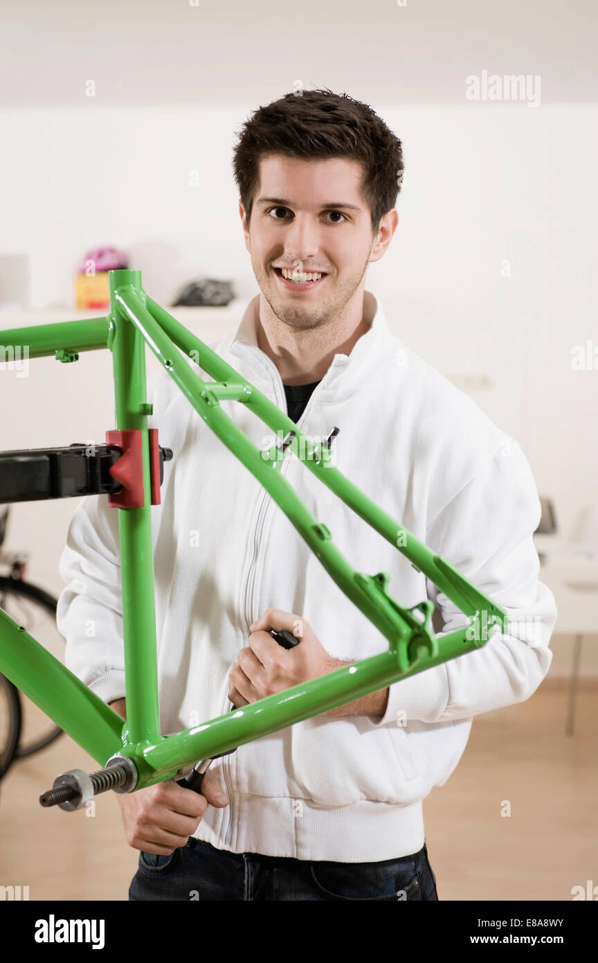 Junger Mann Arbeit am Fahrradrahmen, Lächeln, Porträt Stockfoto