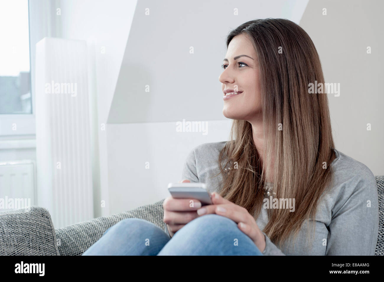 Porträt der lächelnde junge Frau mit Smartphone auf Couch zu Hause Stockfoto