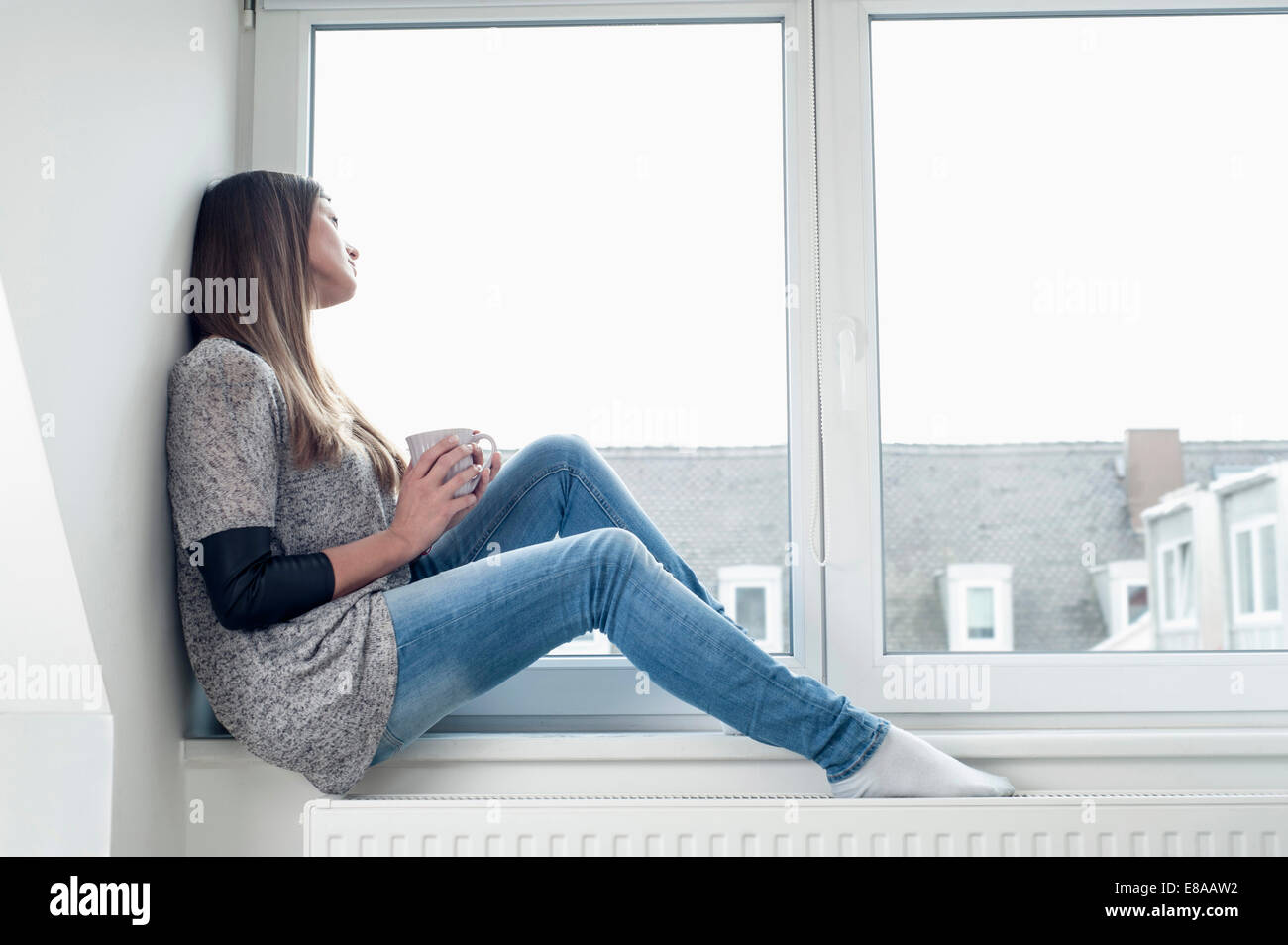 Junge Frau sitzt auf der Fensterbank zu Hause Stockfoto