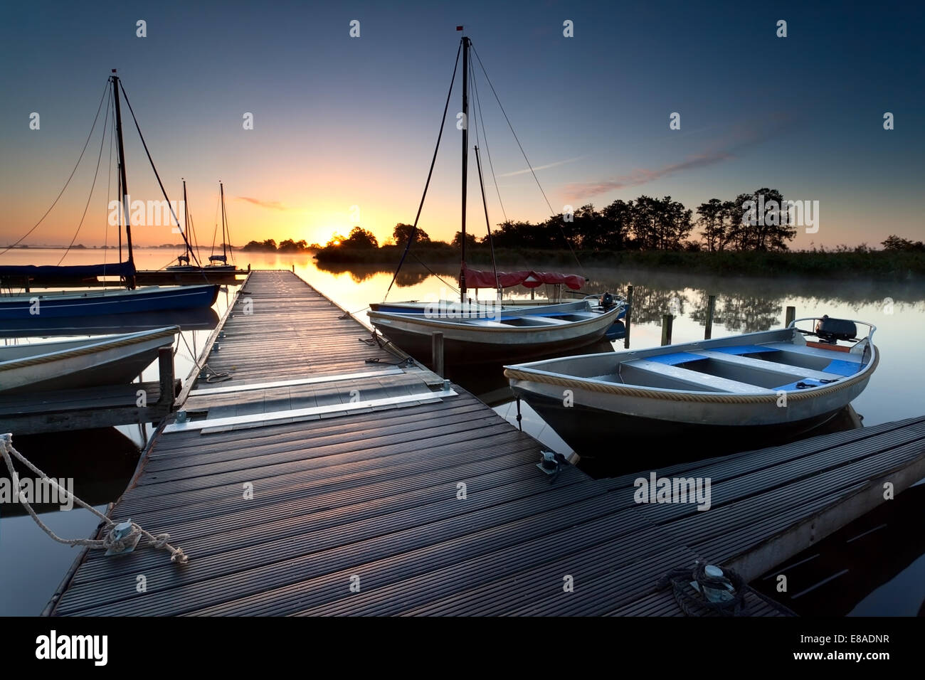 hölzerne Pier und Yachten am großen See bei Sonnenaufgang Stockfoto