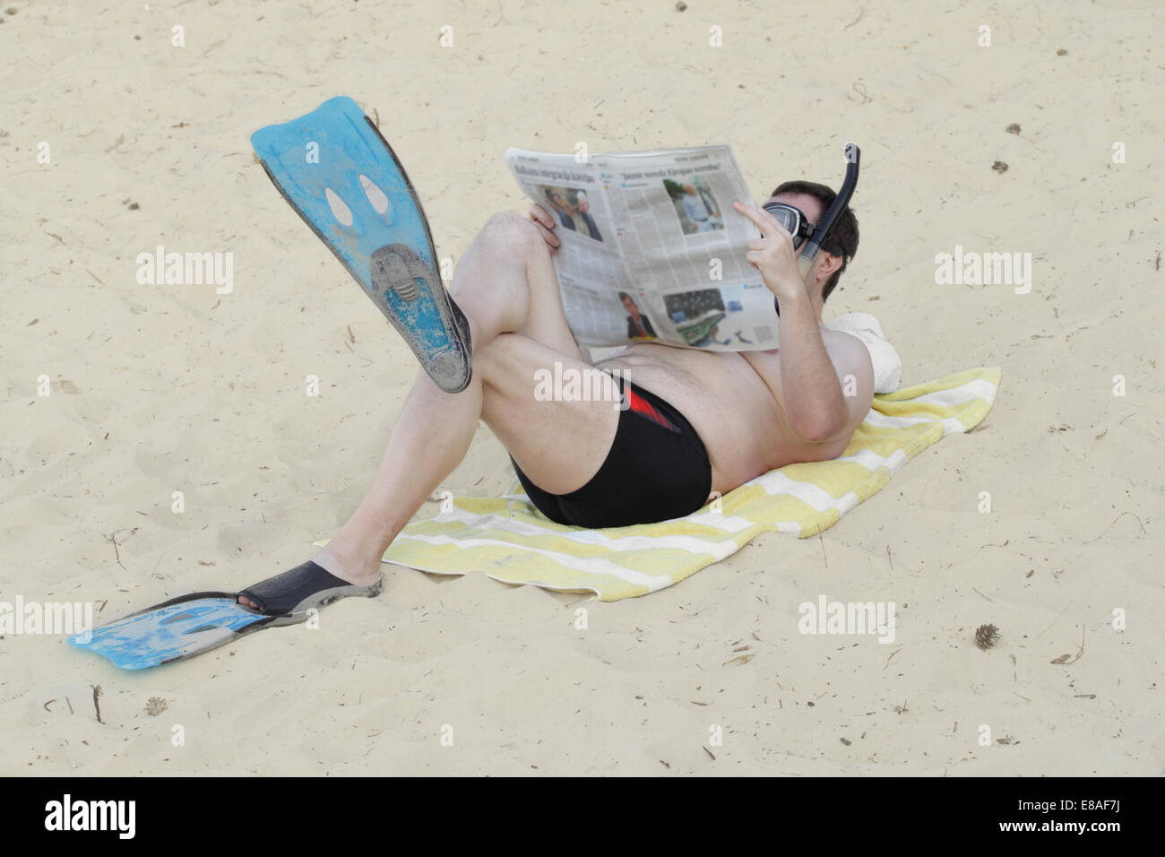Mann in Flossen und Taucherbrille mit Schnorchel legt auf Sand und liest Zeitung Stockfoto