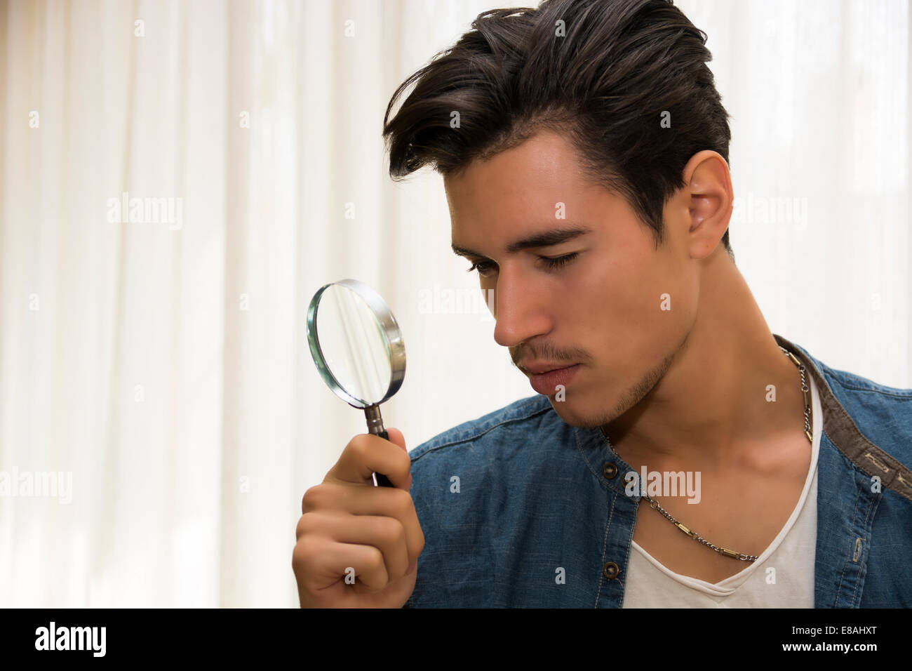 Junger Mann, Blick durch eine Lupe in einem konzeptionellen Bild eines Detektiv auf der Suche nach hinweisen, Inspektion, Prüfung Stockfoto