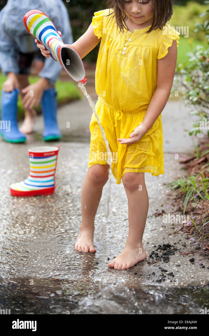Mädchen gießt Wasser aus Kautschuk Stiefel in Regen Pfütze Stockfoto