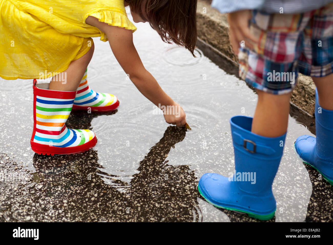 Junge und Schwester tragen Gummistiefel blickte auf in Regen Pfütze Stockfoto