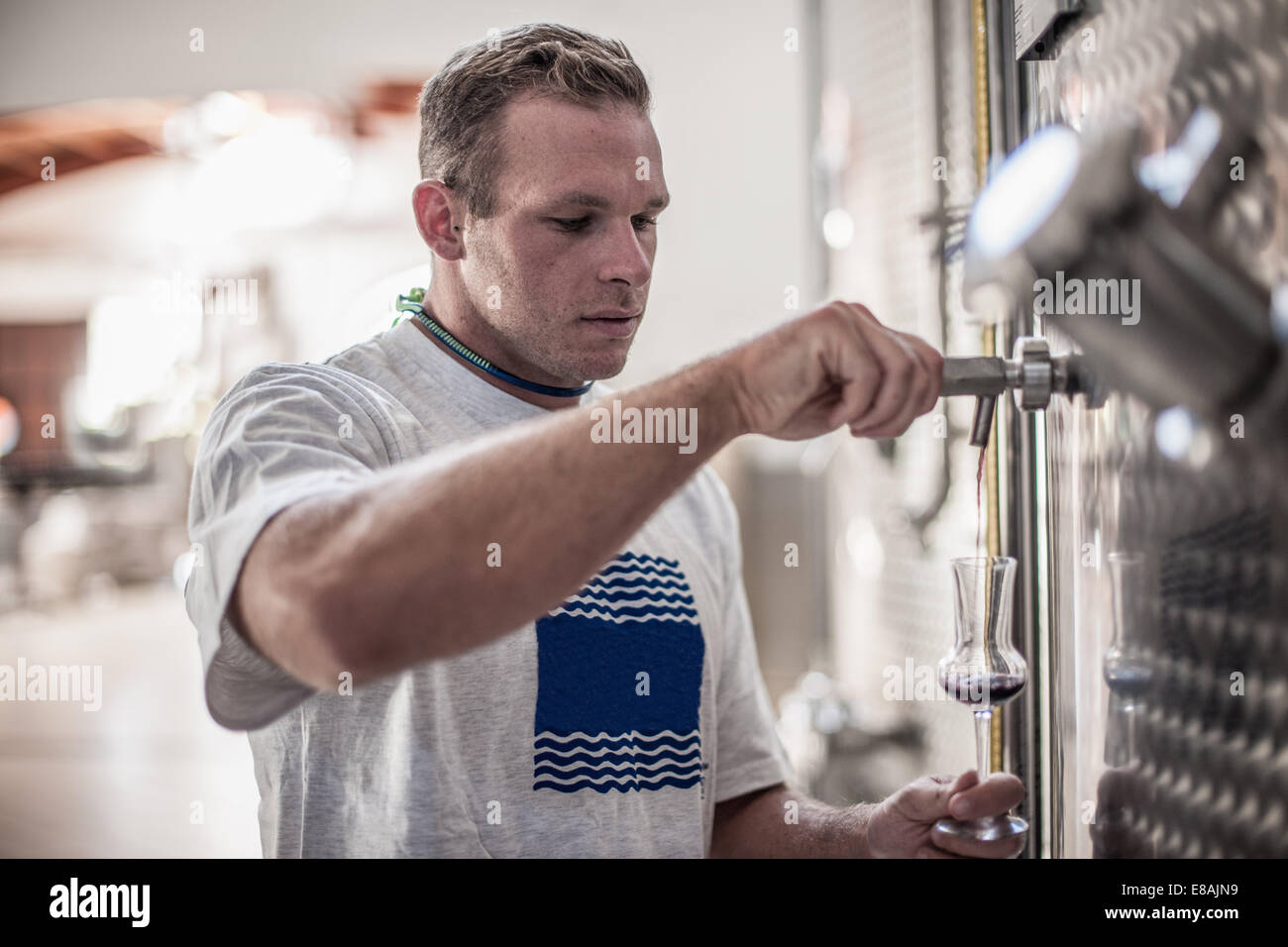 Junger Mann überprüfen Flüssigkeit in stemmed Glas in Fabrik Stockfoto