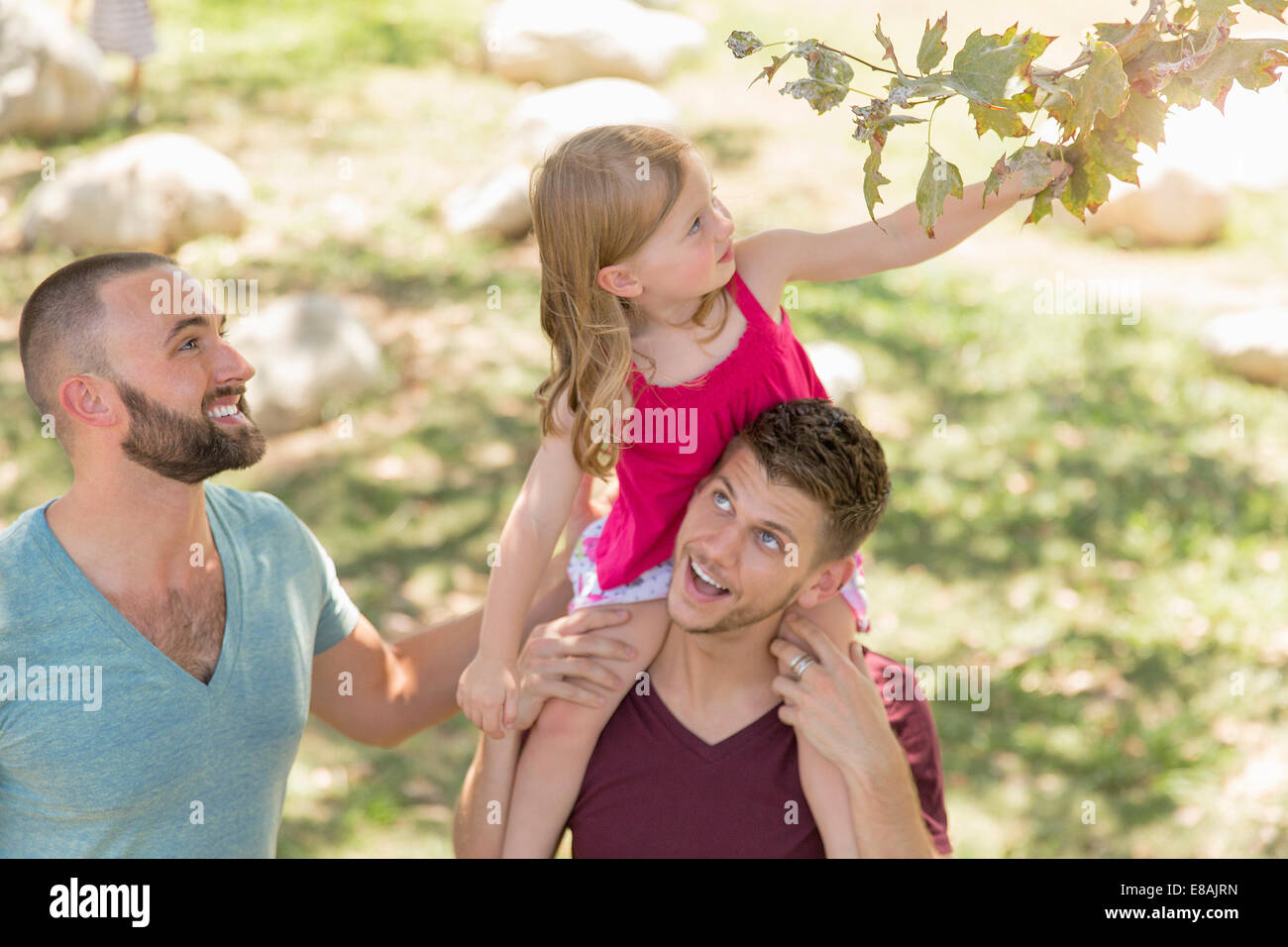 Junge Mädchen sitzen auf Väter Schultern für Baum Blatt im Park zu erreichen Stockfoto