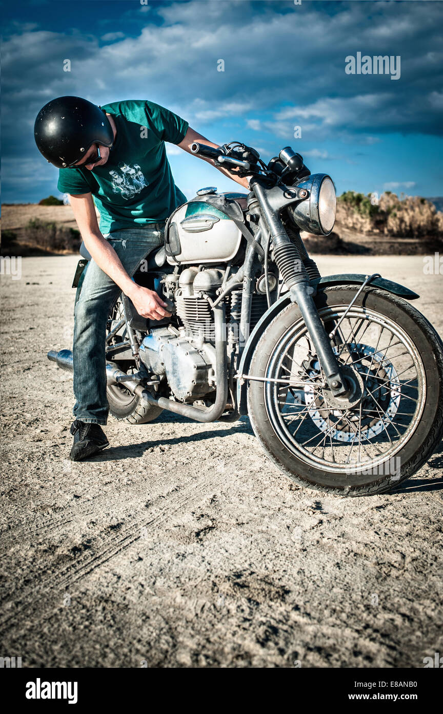 Mitte erwachsenen Mannes Prüfung Motorrad auf trockenen Ebene, Cagliari, Sardinien, Italien Stockfoto