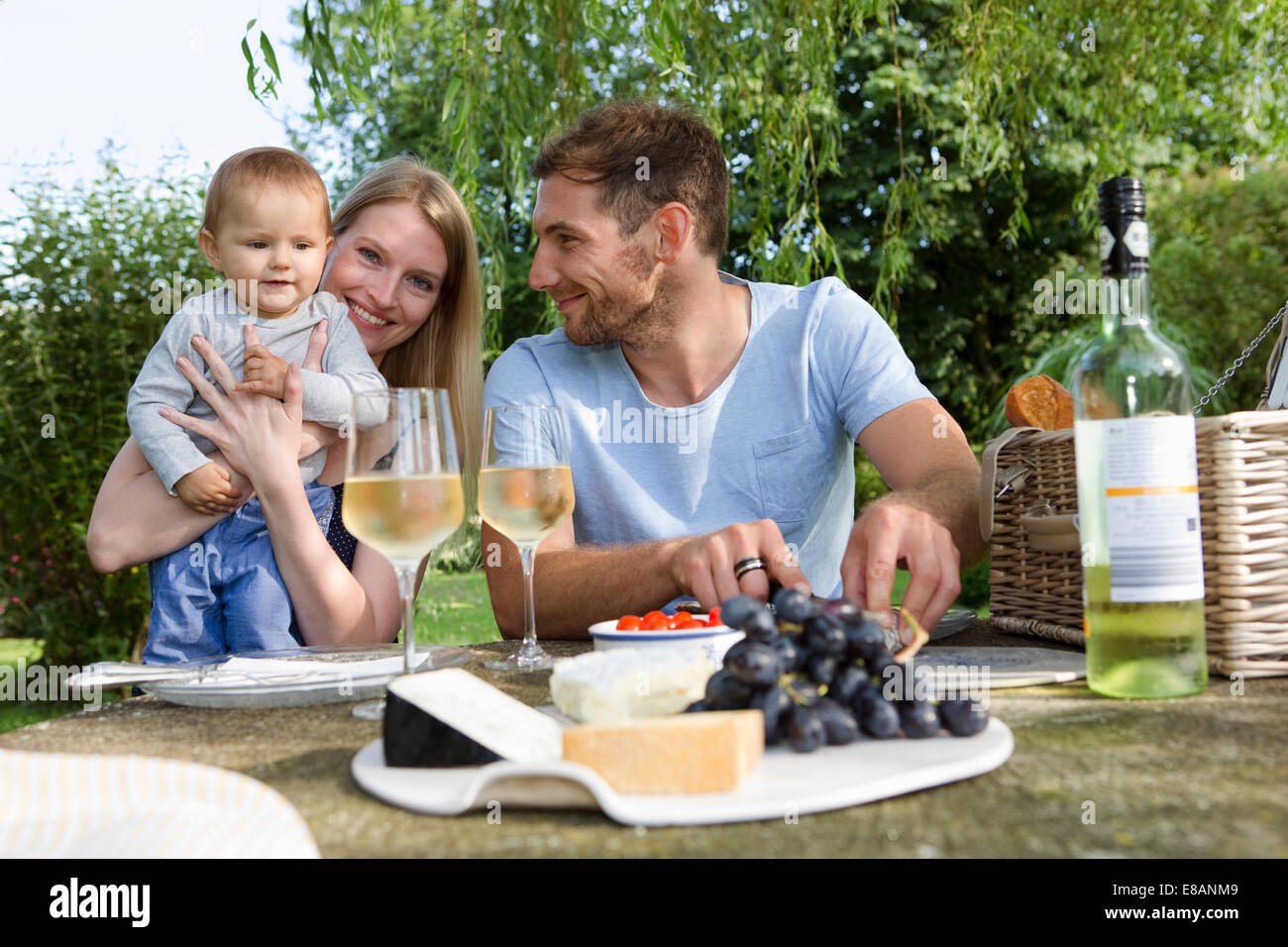 Mitte erwachsenes paar und Tochter sitzen an Picknick-Tisch im Garten Stockfoto