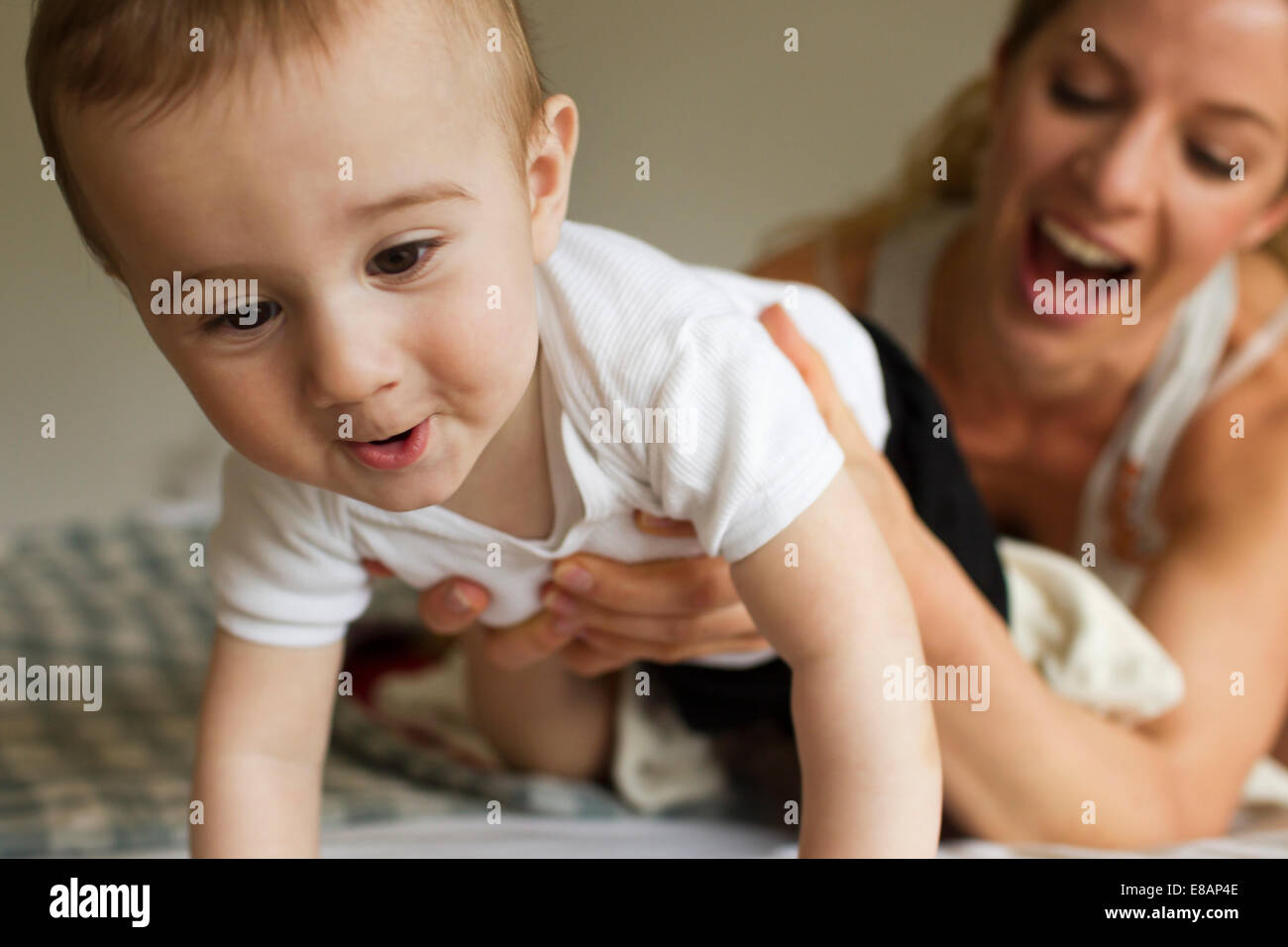Mutter guiding Babyjungen kriechen auf Bett Stockfoto