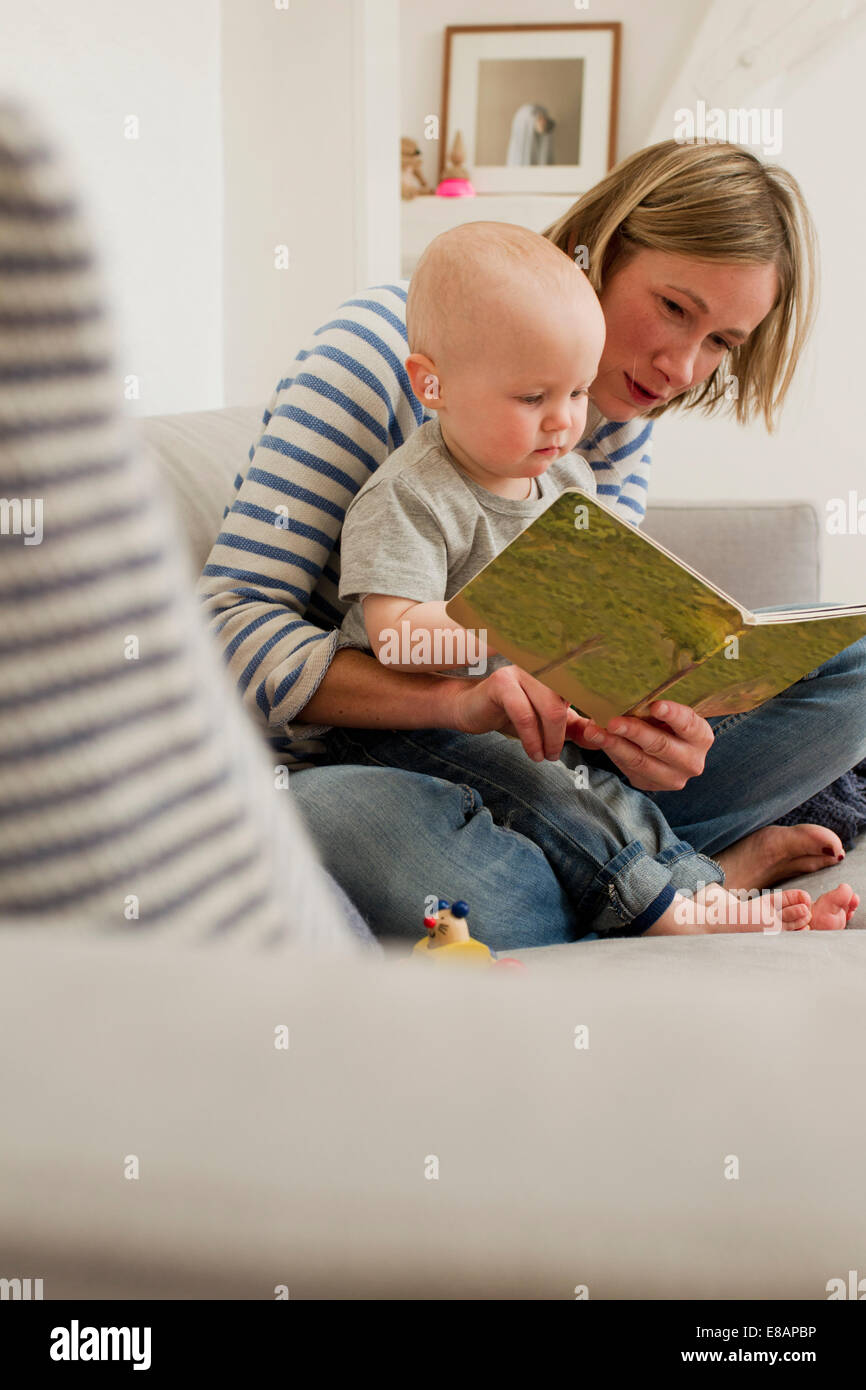 Reife Mutter lesen Storybook Baby Tochter auf Wohnzimmer-sofa Stockfoto