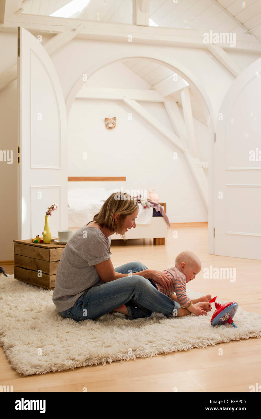 Reife Mutter und Baby Tochter spielen auf Teppich im Wohnzimmer Stockfoto