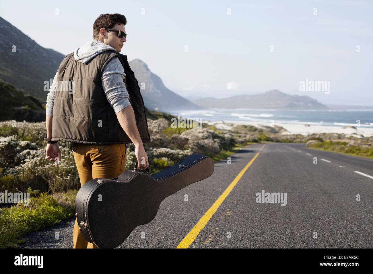 Rückansicht des jungen Mann zu Fuß auf der Küstenstraße mit Gitarre Fall, Cape Town, Western Cape, Südafrika Stockfoto