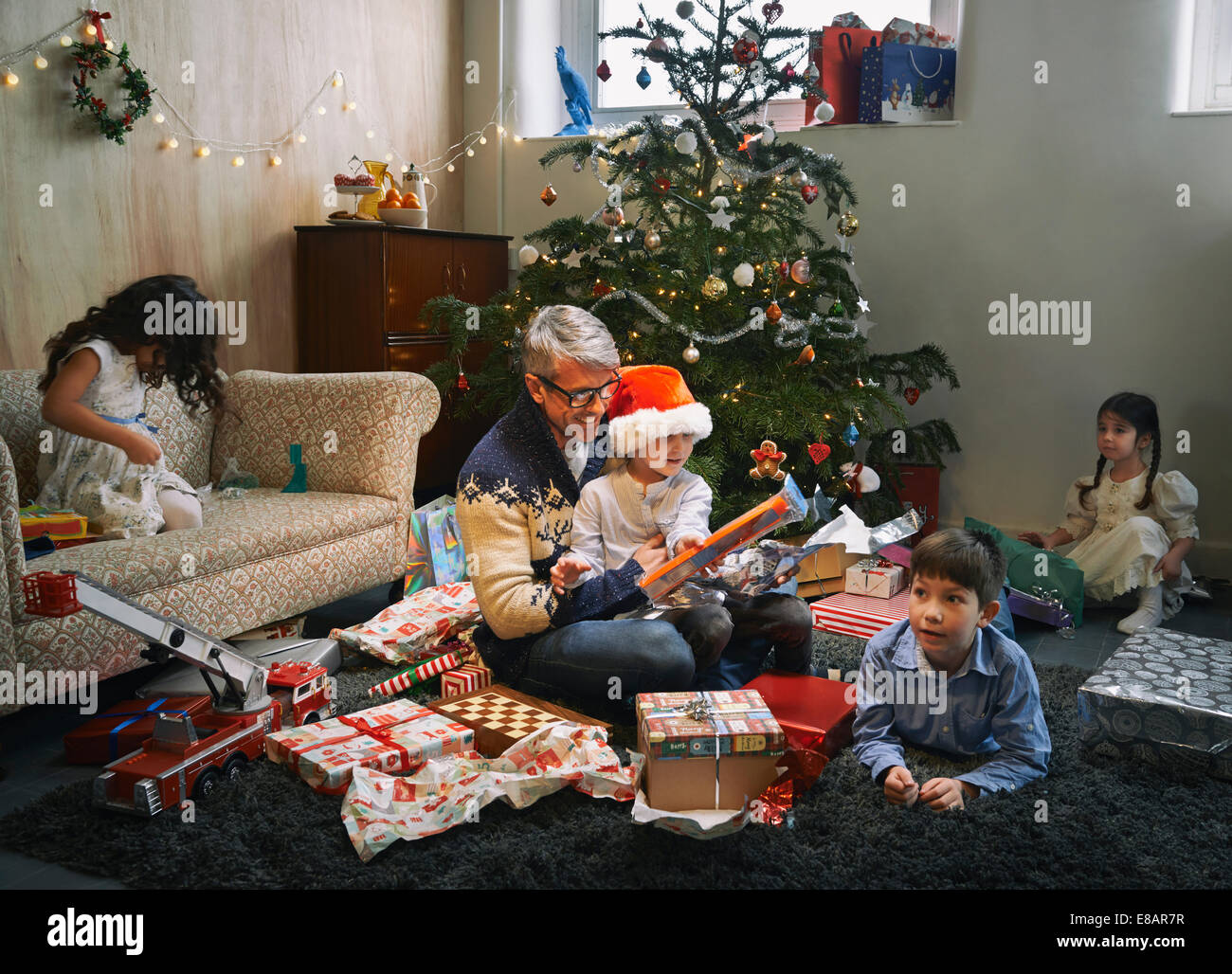 Vater und seinen vier Kindern Weihnachtsgeschenke im Wohnzimmer öffnen Stockfoto
