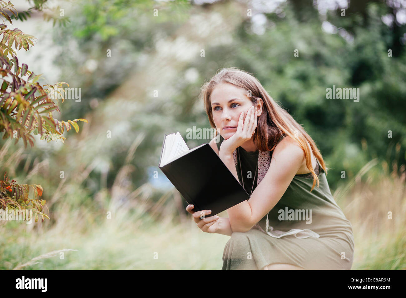 Junge Frau mit Kinn auf Hand Buch im Bereich Stockfoto