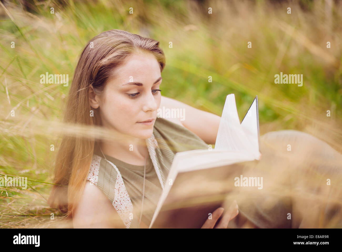 Junge Frau sitzt in lange Grashalme Buch Stockfoto