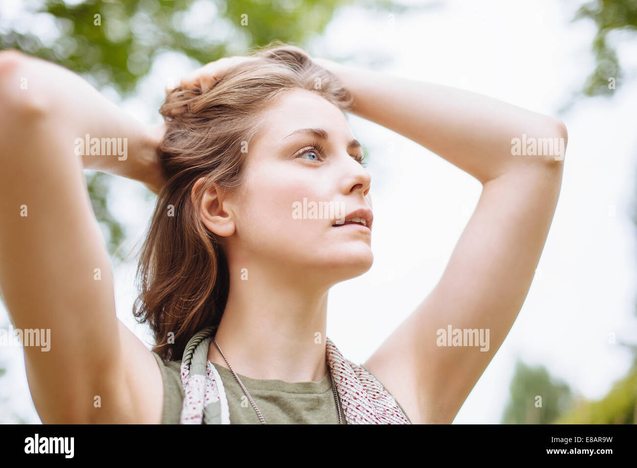 Ruhige junge Frau blickte mit Händen in Haar Stockfoto