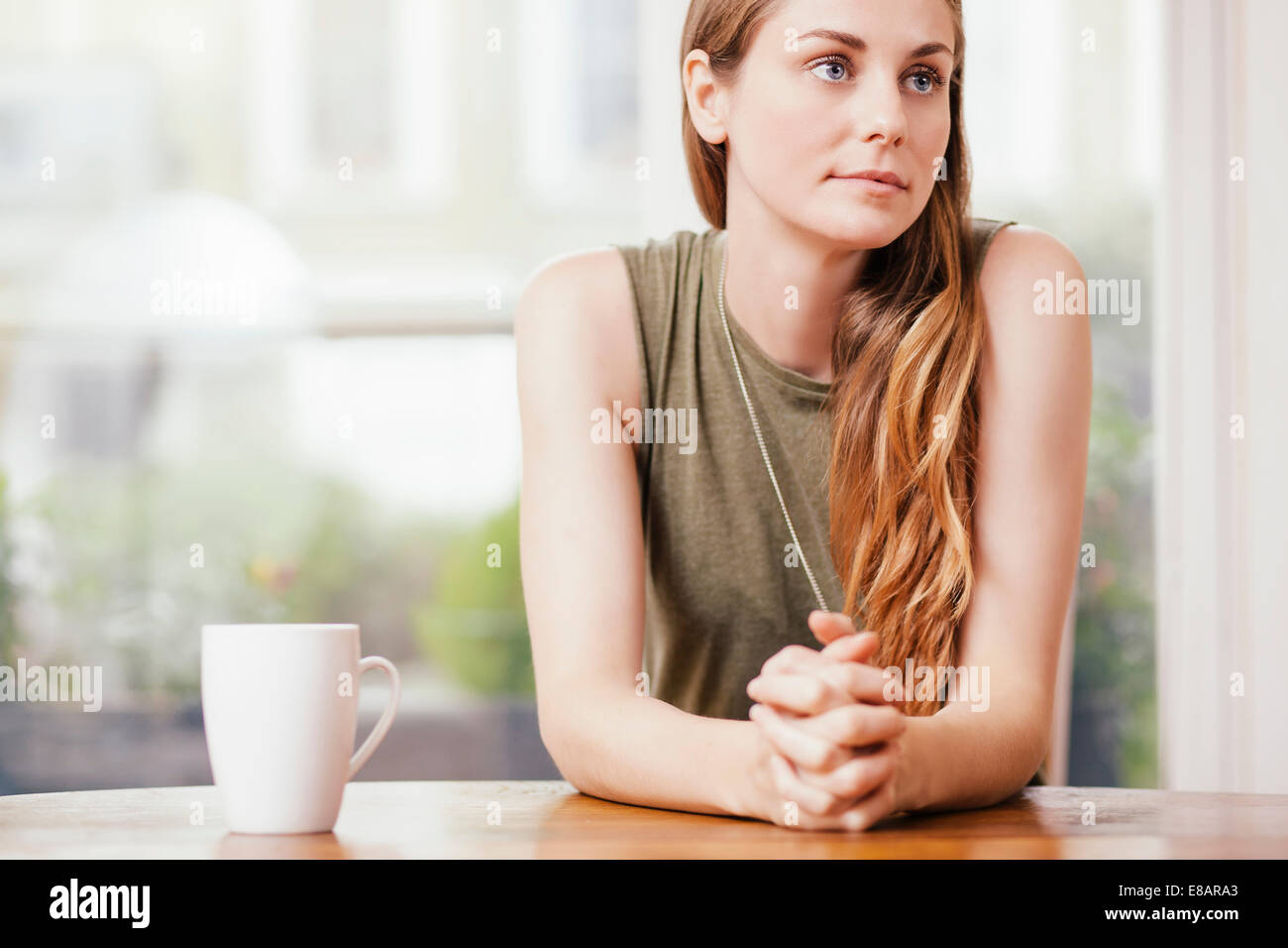 Junge Frau mit den Händen umklammert am Esstisch sitzen Stockfoto