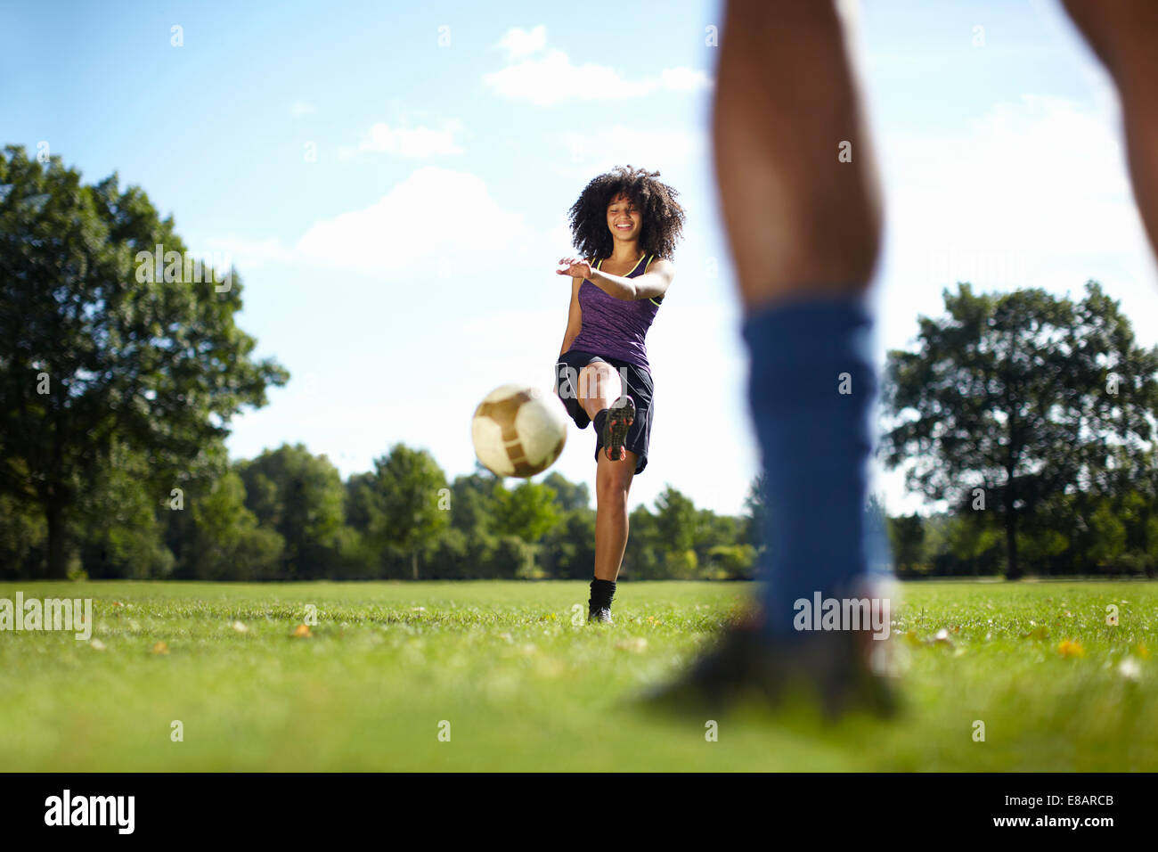 Junge Frau treten Fußball in Richtung Freund im park Stockfoto