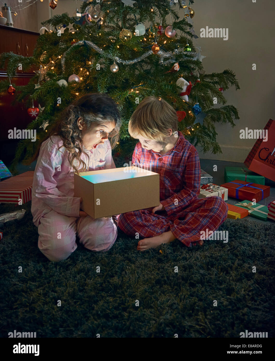 Schwester und Bruder öffnen Mund auf Auspacken leuchtende Weihnachts-Geschenk-box Stockfoto