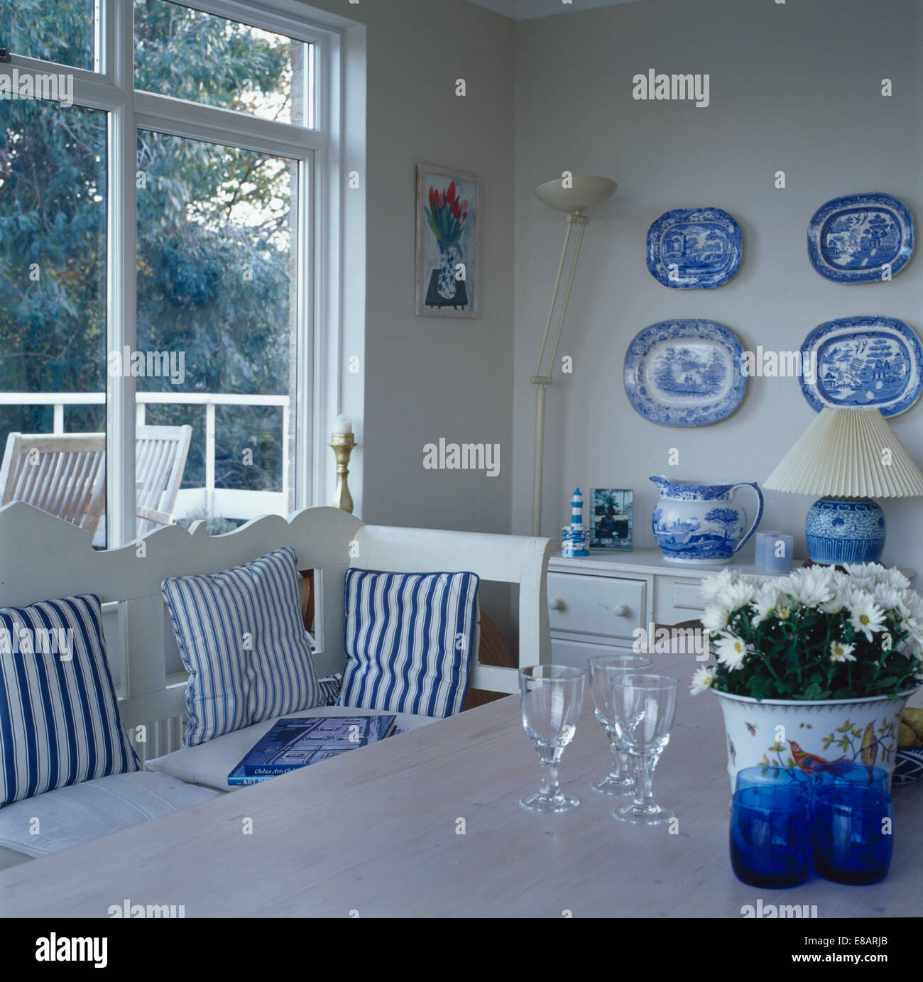 Sammlung von blaue + weiße Platten an Wand des Esszimmers mit blau gestreiften Kissen auf weißen Settle vor Fenster Stockfoto