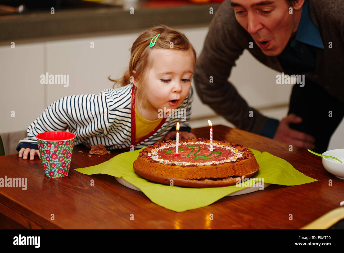 Junges Mädchen bläst Geburtstagskerzen auf Kuchen Stockfoto
