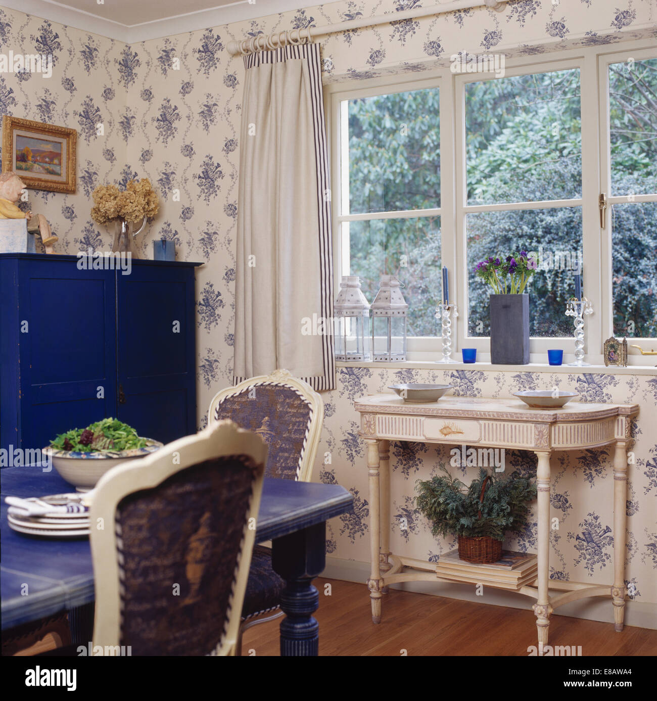 Weiß lackiertes Konsolentisch unter Fenster im Land Speisesaal mit blau + weiß floral Tapete Stockfoto
