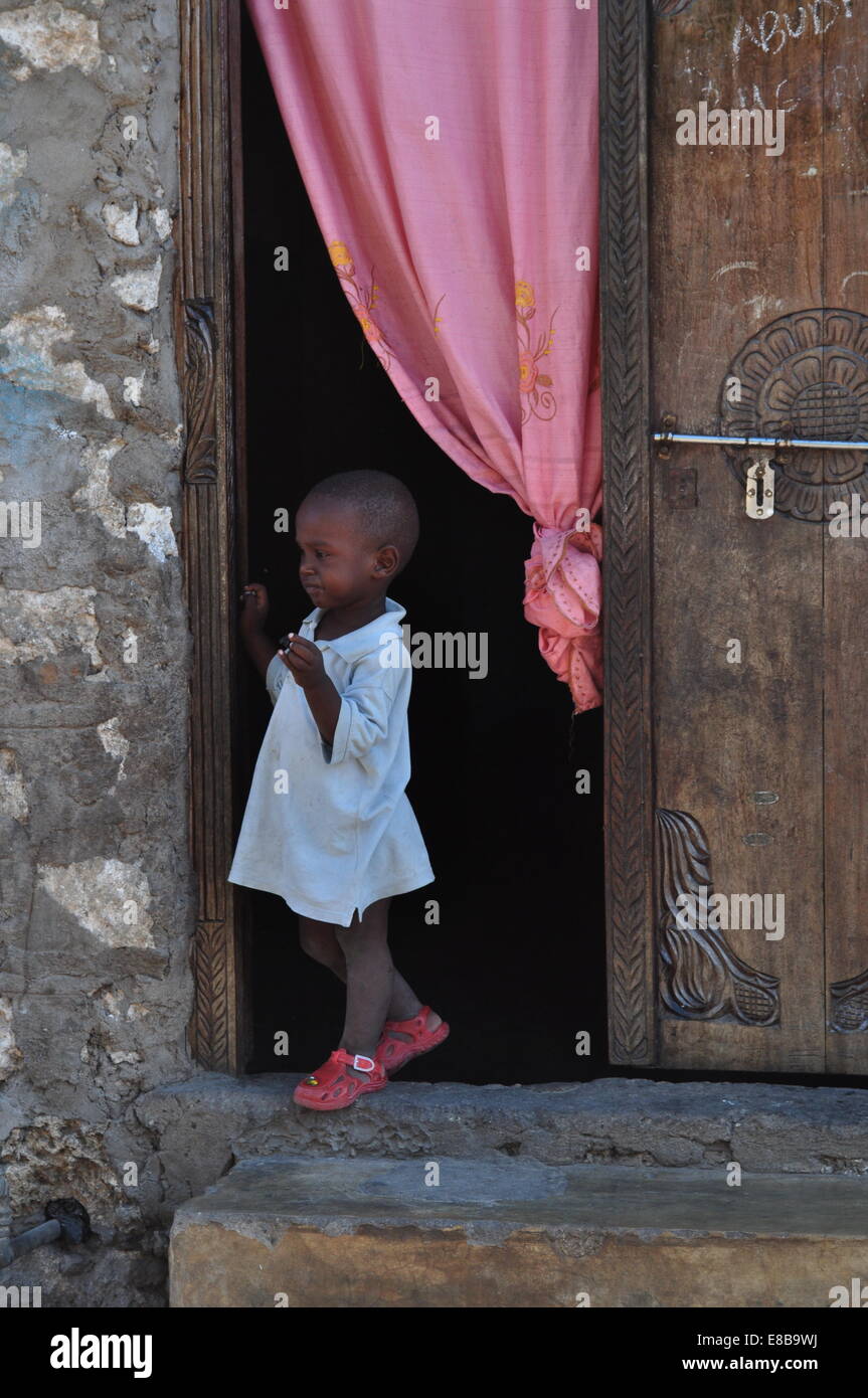 Ein kleines Mädchen essen einen Keks vor Haustür in den Straßen von Watamu, Kenia Stockfoto
