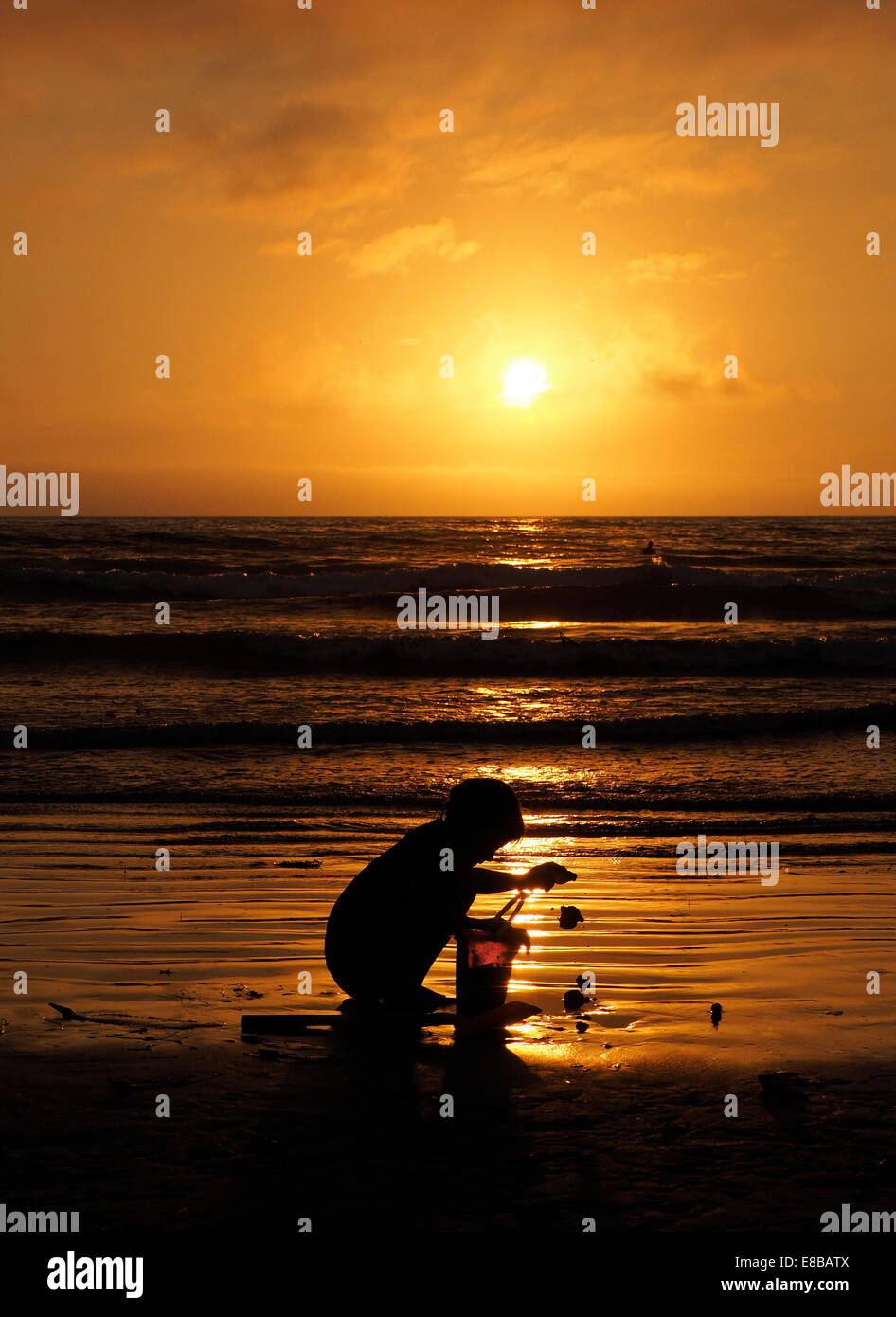 Young Boy spielen mit einem Eimer auf nassen Sand bei Sonnenuntergang Stockfoto