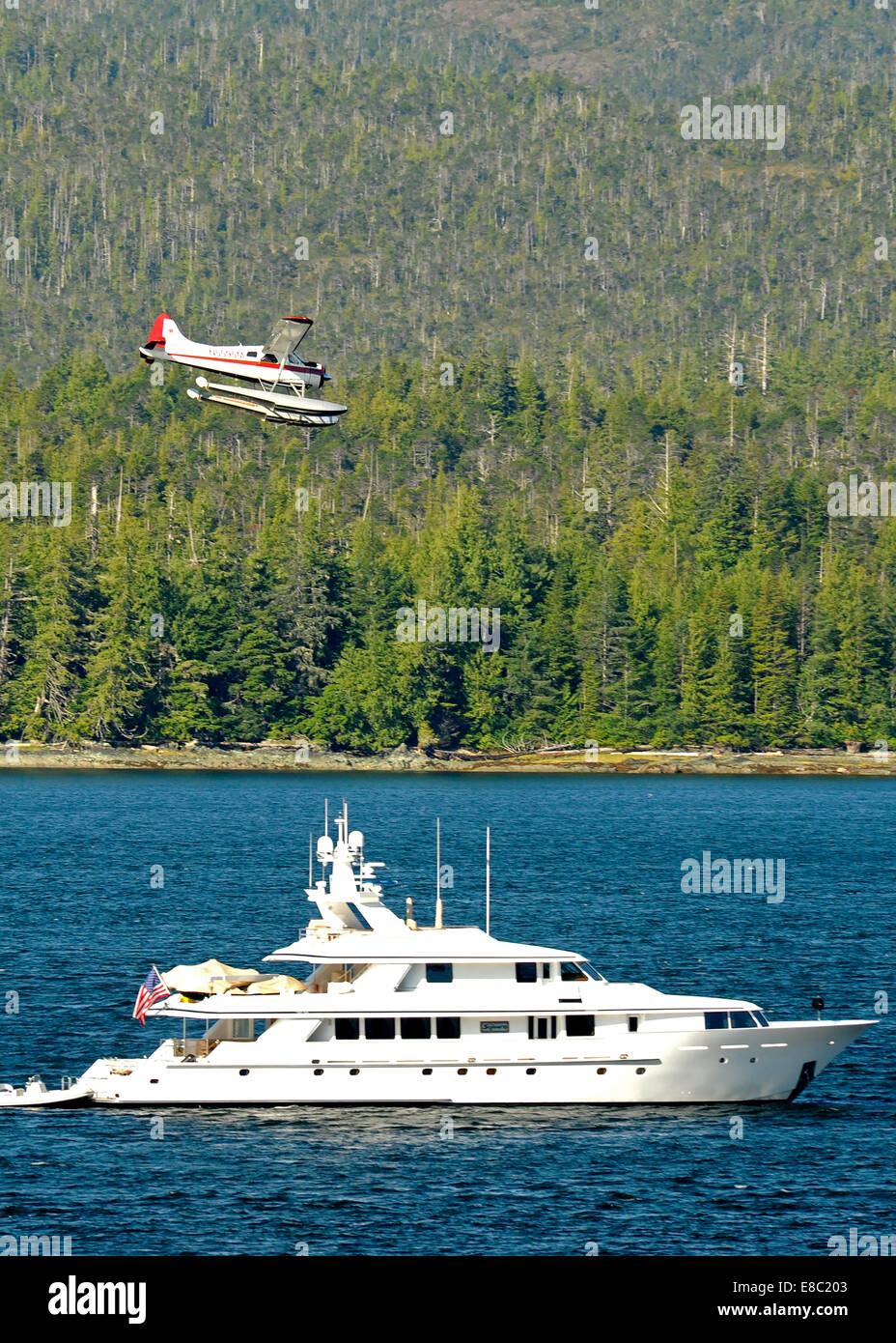 Ein Wasserflugzeug/Sea Plane kommt für eine Landung in der Baumgrenze und oben eine große Yacht in Alaska. Stockfoto