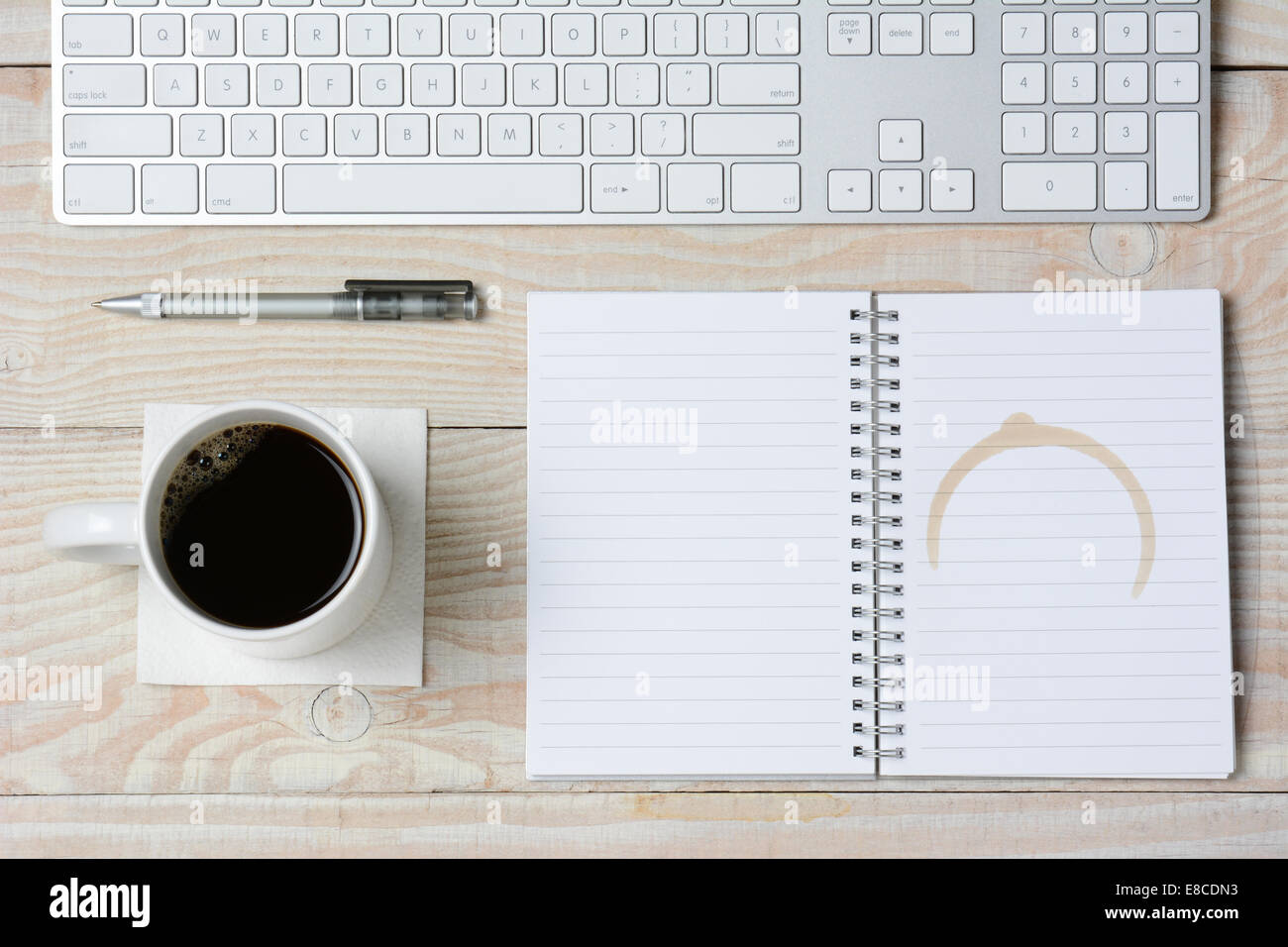 Hohen Winkel Schuss aus einem weißen rustikalen Schreibtisch mit modernen Tastatur, Kaffeetasse und Notebook mit einem Kaffeefleck. Querformat. Stockfoto