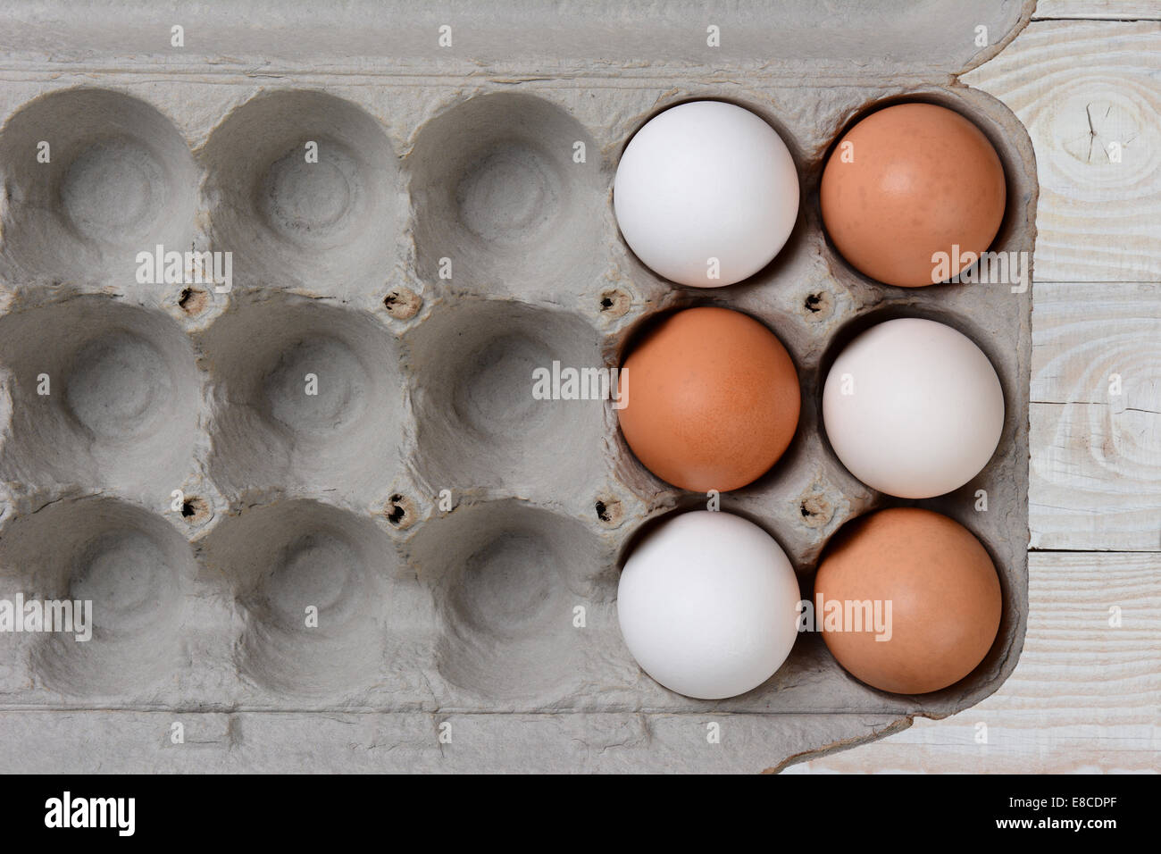 Sechs Eiern, drei weißen und drei braune, in einem großen Karton mit leeren Räumen. Der Karton ist auf eine weiße Landhaus-Küche Stockfoto
