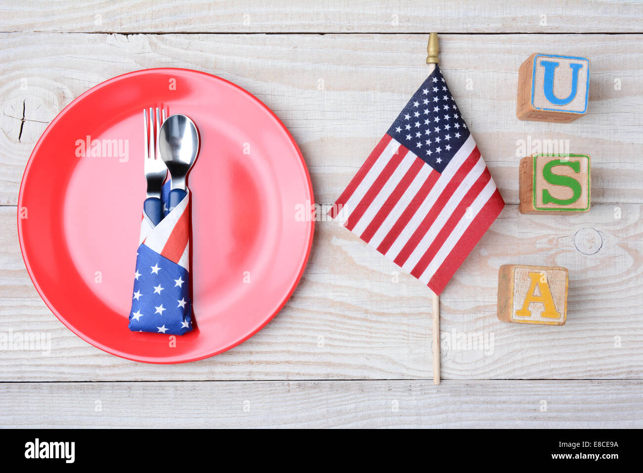 Ein Picknick-Tisch für ein 4. Juli Picknick bereit. Eine rote Platte mit Gabel und Löffel, amerikanische Flagge und Blöcke, die Rechtschreibung aus USA. Stockfoto