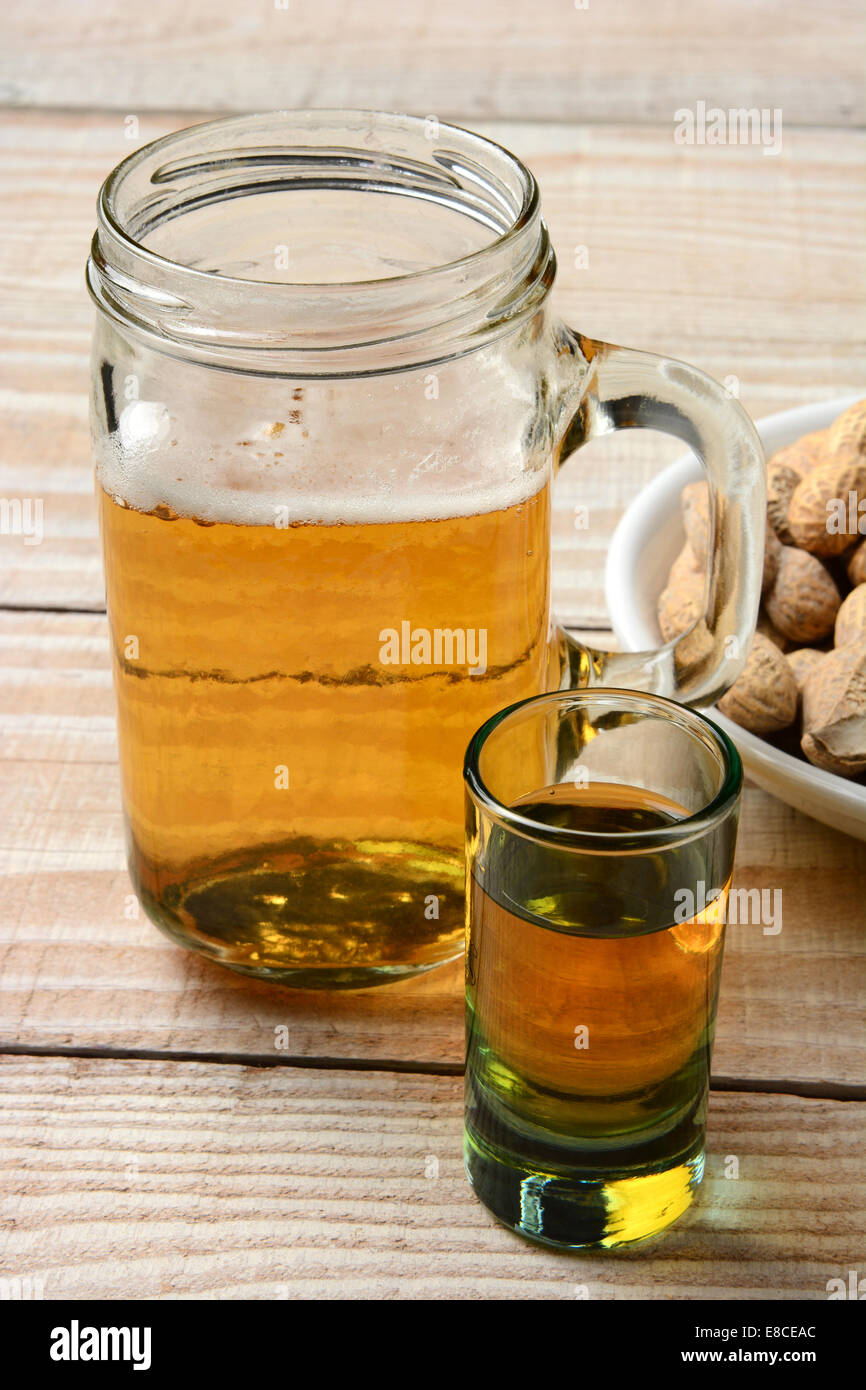 Nahaufnahme von einem Schuss Whisky, eine Maß Bier und eine Schale mit Erdnüssen. Hochformat auf einem rustikalen Holztisch. Stockfoto