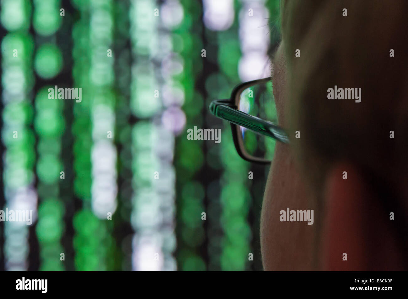 Ein junger Mann mit Brille sieht futuristisch Symbole auf einem Computerbildschirm. Stockfoto