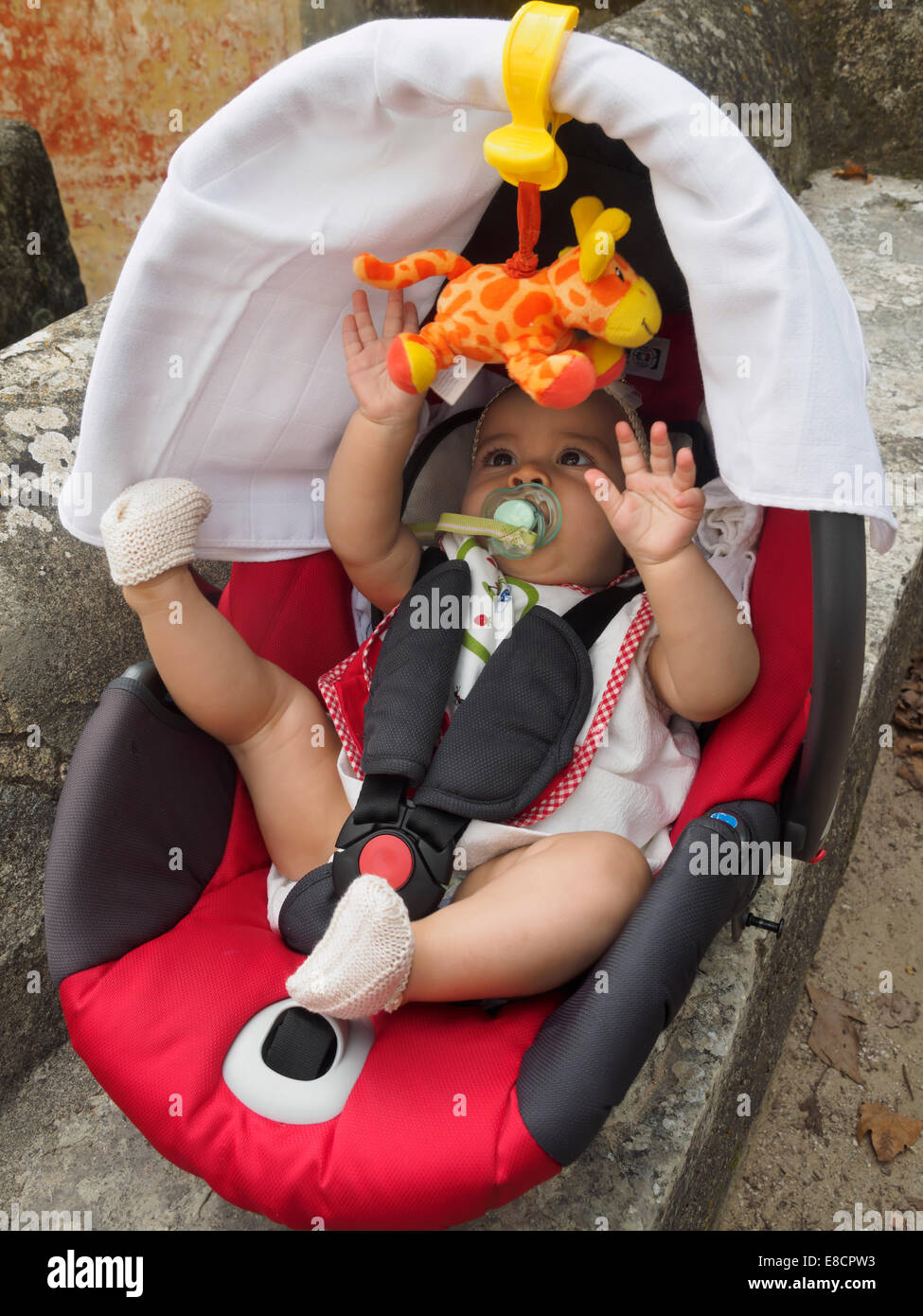 Baby spielt mit Spielzeug Giraffe, während in einem Kindersitz angeschnallt Stockfoto