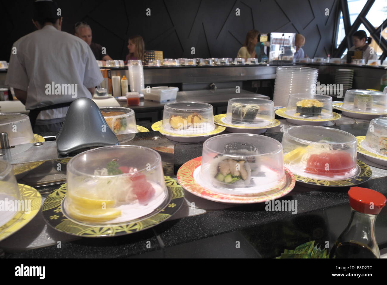 japanisches Sushi-Zug-Restaurant im Norden von Sydney, Australien, Sushi-Essen auf überdachten Tellern mit Koch im Hintergrund. Stockfoto