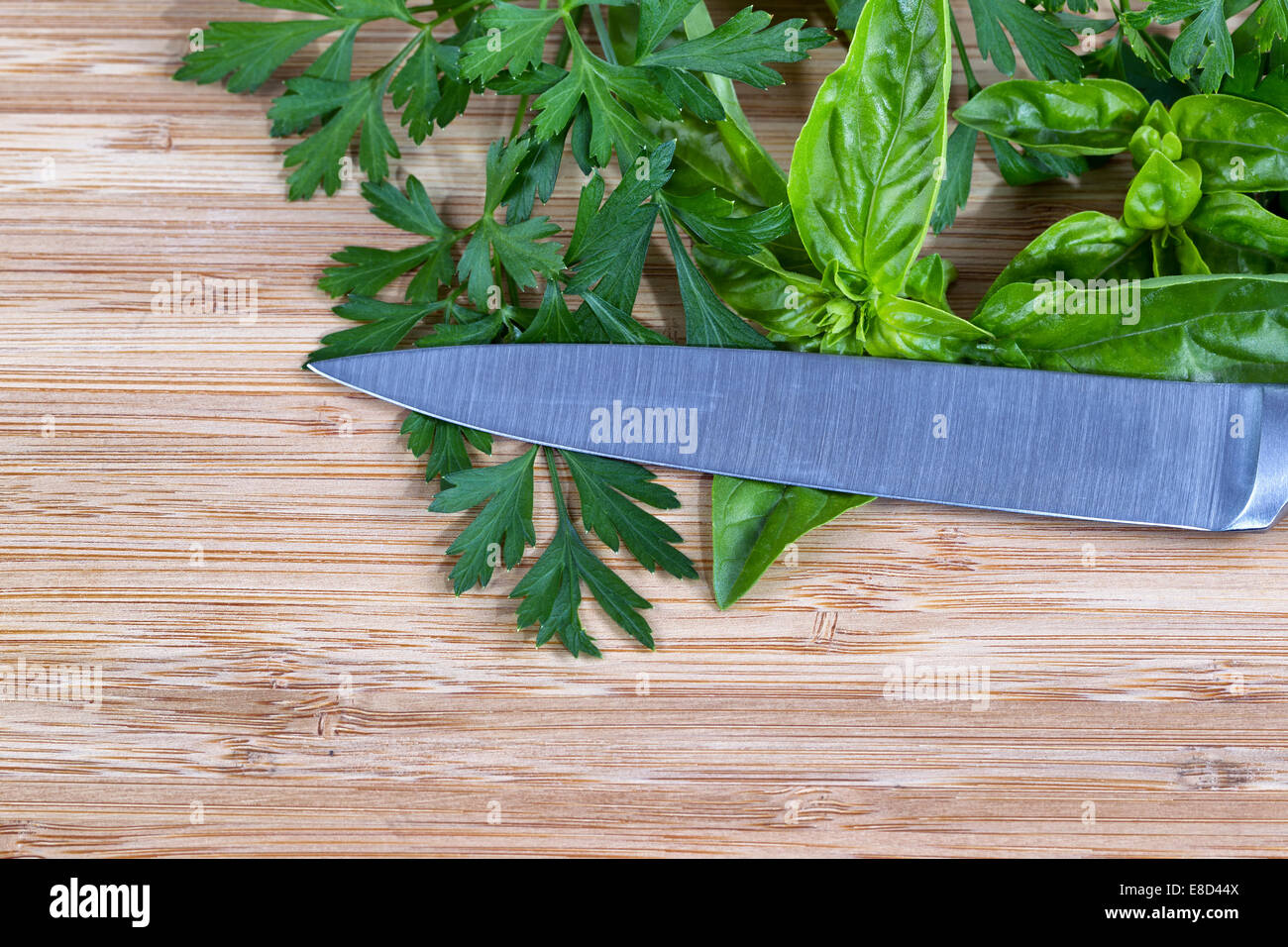 Horizontale Draufsicht von frischem Basilikum und Petersilie mit Messer auf natürlichem Bambus Holz Schneidebrett Stockfoto