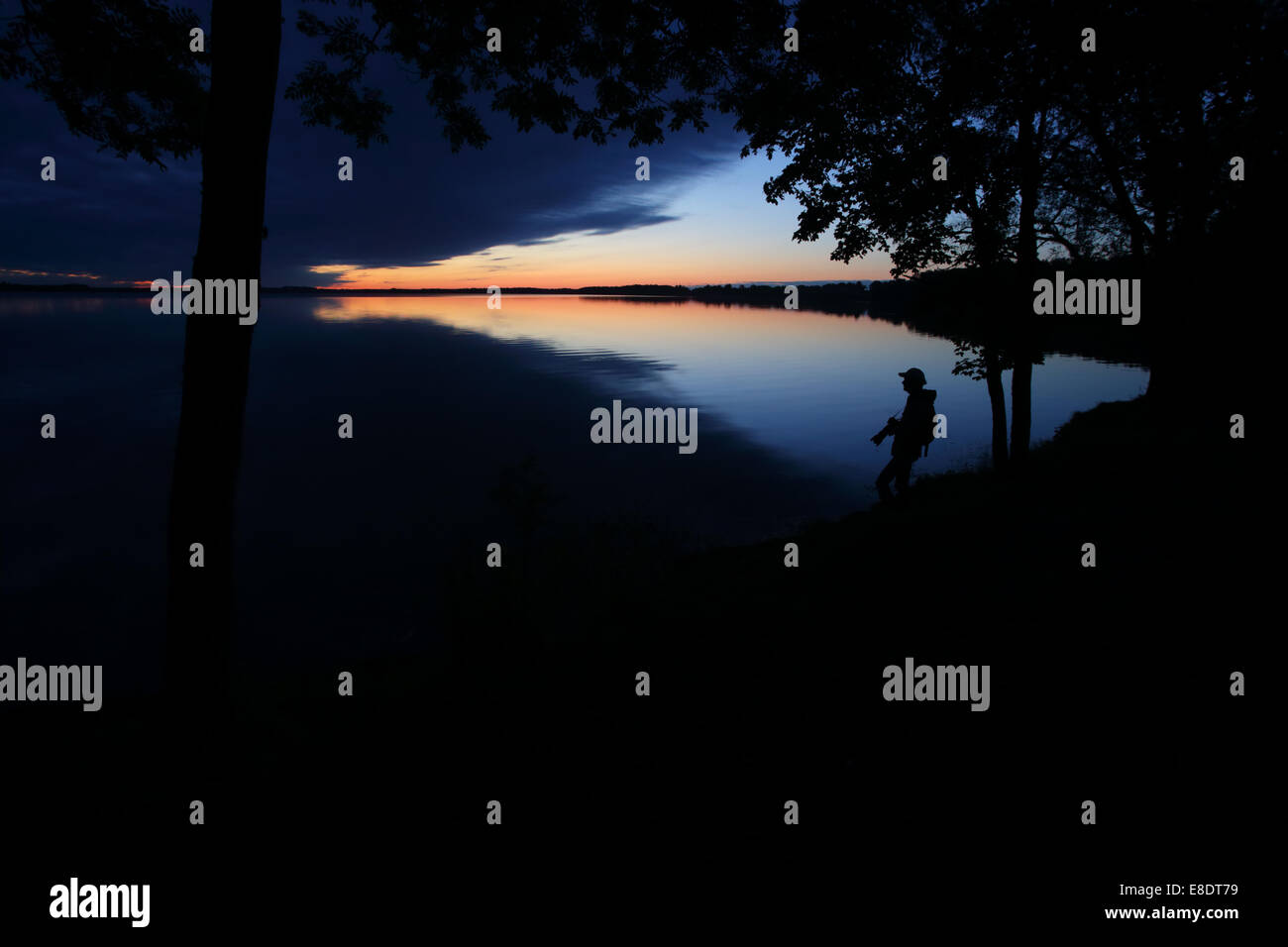 Der Naturfotograf mit Kamera stehend am See zur blauen Stunde, nach dem Sonnenuntergang Stockfoto