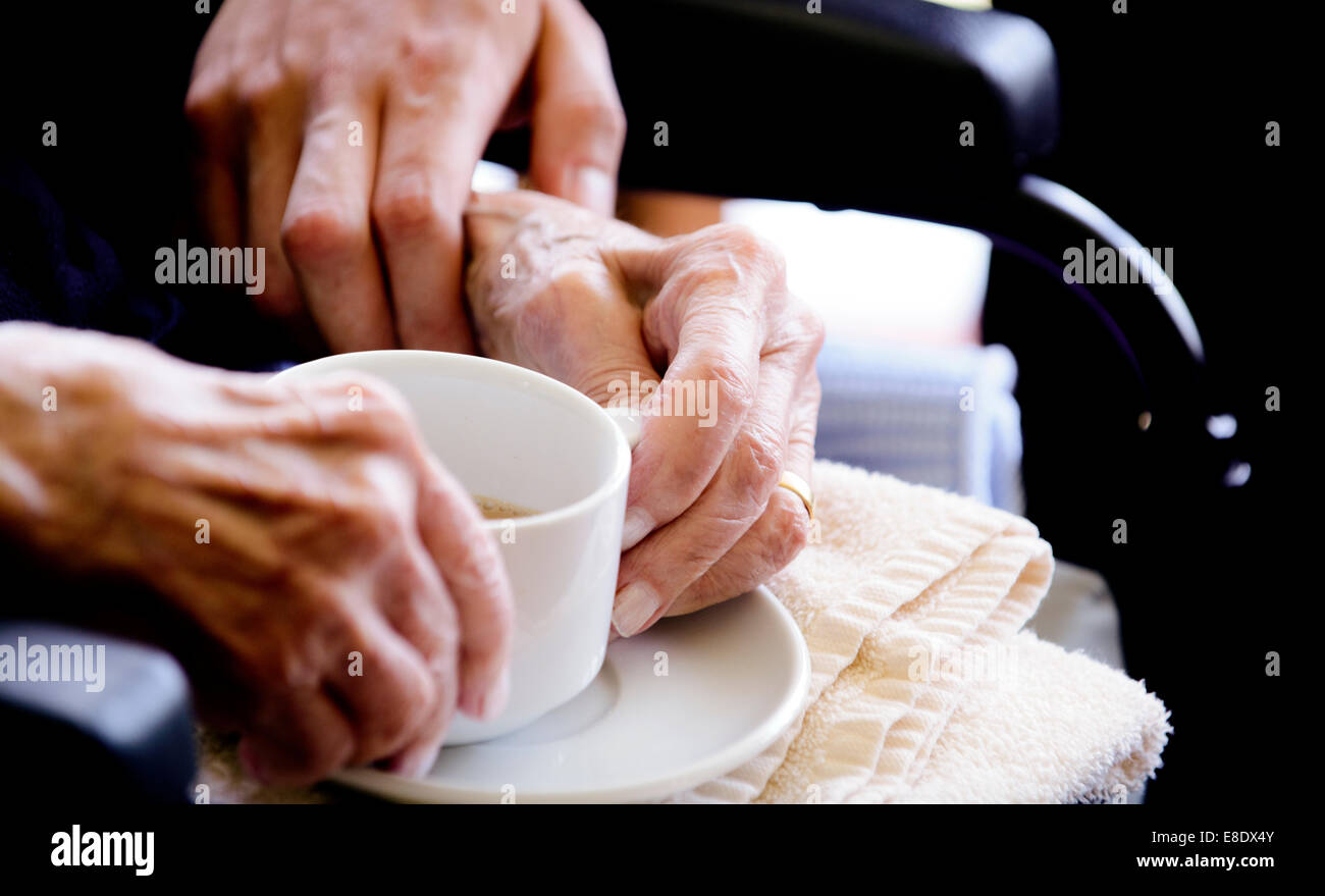 Eine ältere Person in einem Rollstuhl sitzt ist eine Tasse Tee von Pflegepersonal übergeben. Stockfoto