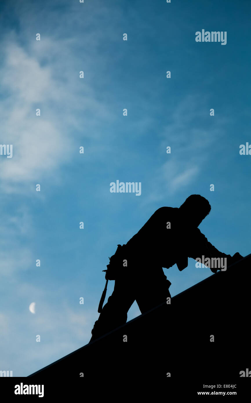 Auftragnehmer im Silhouette arbeiten auf einem Dach mit blauen Himmel im Hintergrund Stockfoto