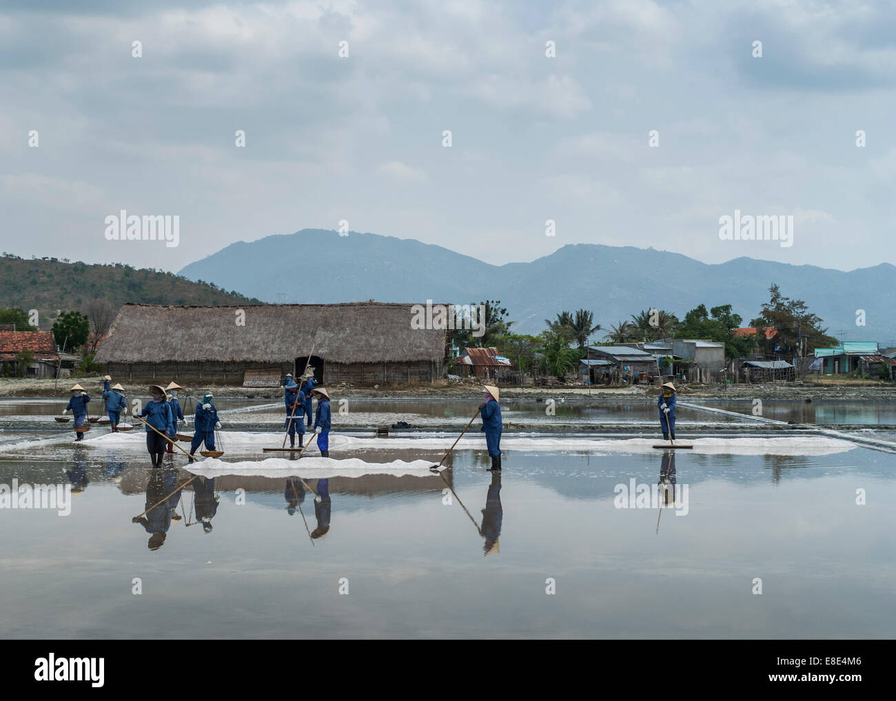 Süd-Vietnam - März 2012: Crew blau gekleidete Menschen Harke, Schaufel und tragen Körbe frisch geerntete Salz. Stockfoto