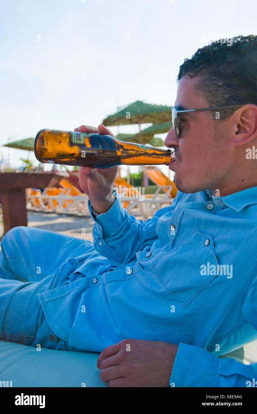 Vertikale Porträt eines jungen attraktiven marokkanischen Mannes ein Bier am Strand trinken. Stockfoto